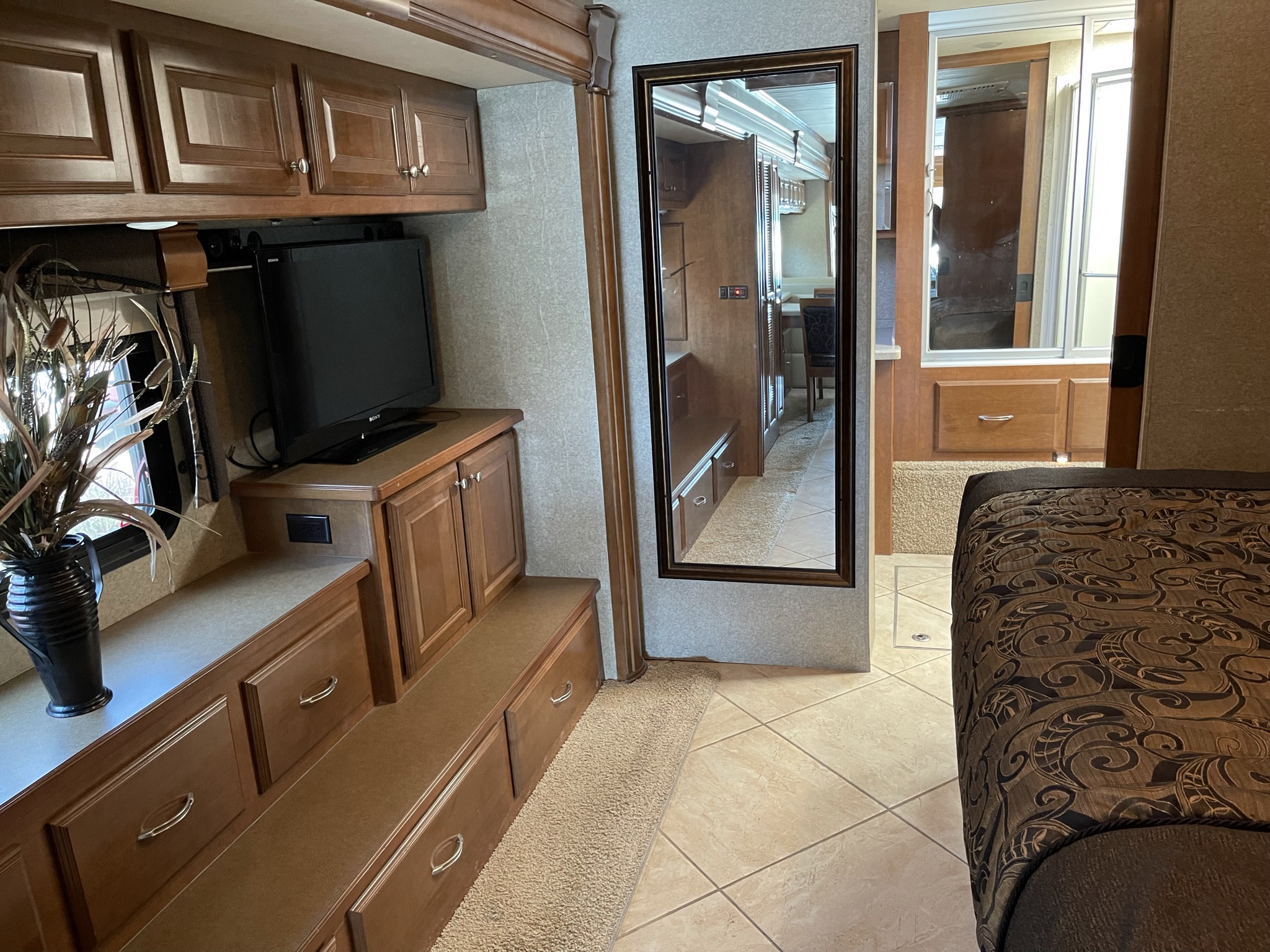 This RV rental interior showcases a living room with TV, cabinetry, and a cozy bedroom. The mirror reflects a dining area.. Thor Tuscany XTE 2014