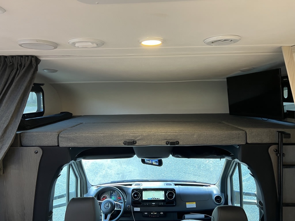 Spacious cab-over bed and cockpit of an RV rental, featuring a TV and comfortable sleeping area.. Forest River Sunseeker MBS 2023
