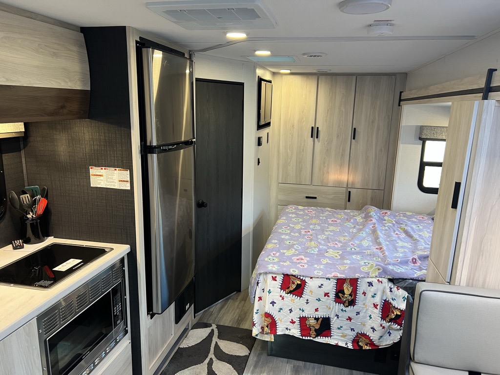 Spacious RV rental interior featuring a full kitchen with fridge & microwave, plus a cozy bedroom area. Ideal for travel.. Forest River Sunseeker MBS 2023