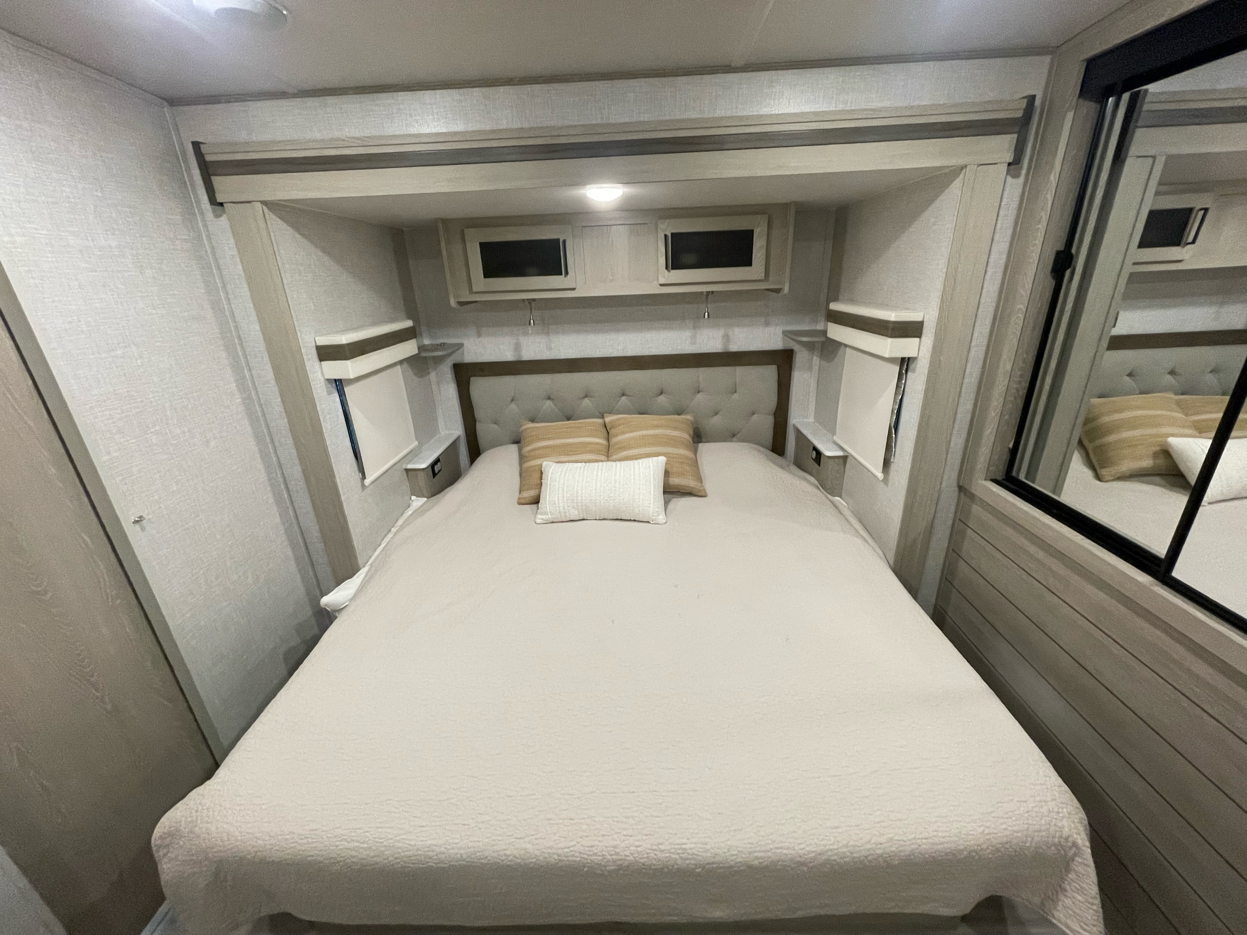 This cozy RV rental bedroom offers a comfortable bed, overhead storage, and a modern, neutral design for travel comfort.. Forest River Rockwood Signature 2022