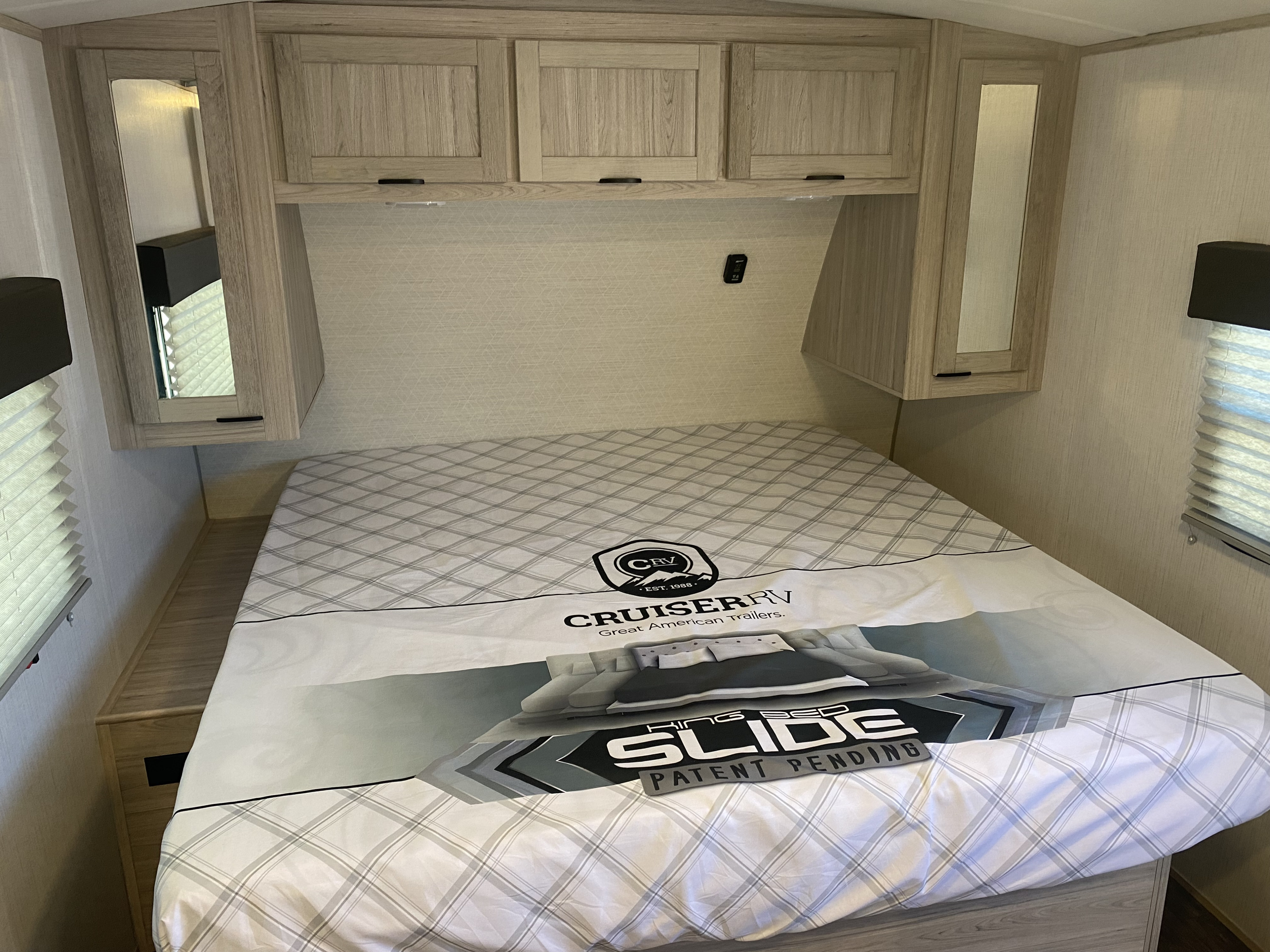Cozy RV rental bedroom: bed with "King Bed Slide" graphic, light wood overhead cabinets & mirrored storage.. Heartland SHADOW CRUISER 215RBS 2022