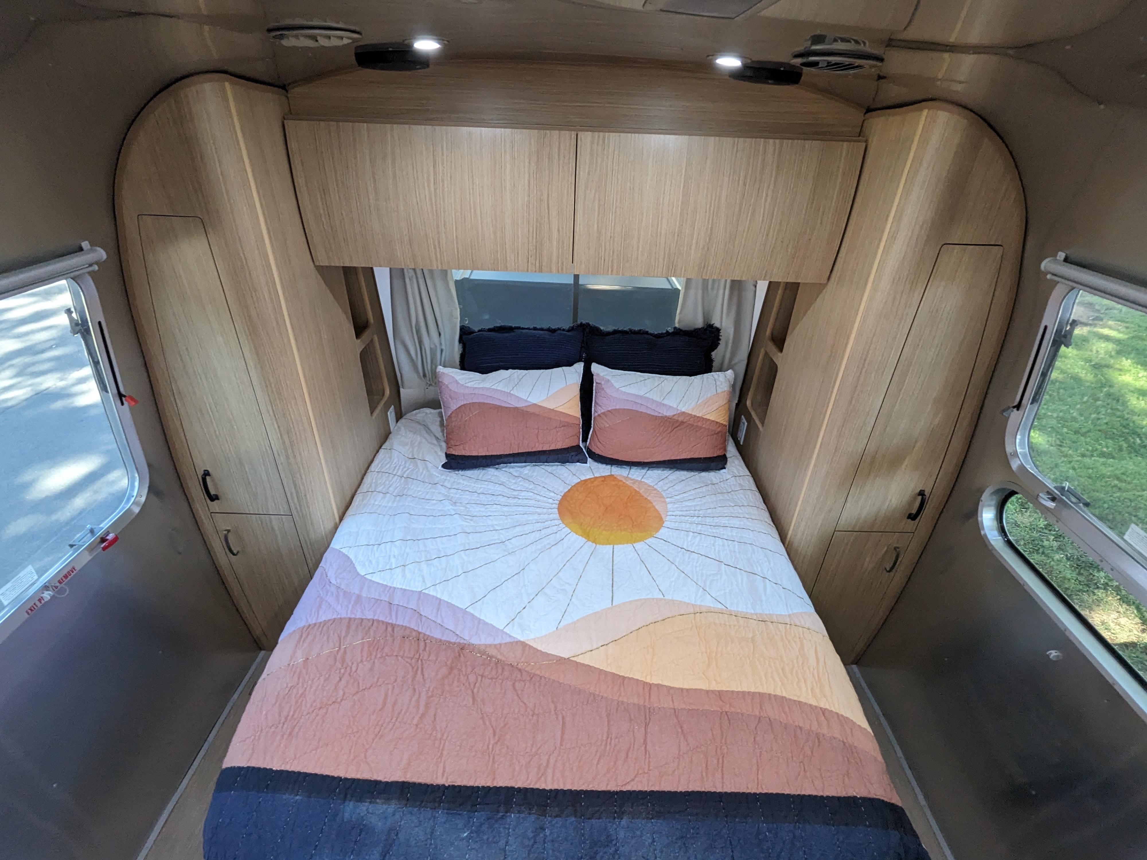 Cozy RV rental bedroom featuring a bed with a colorful quilt, built-in cabinets, and bright side windows.. Airstream Flying Cloud 2020