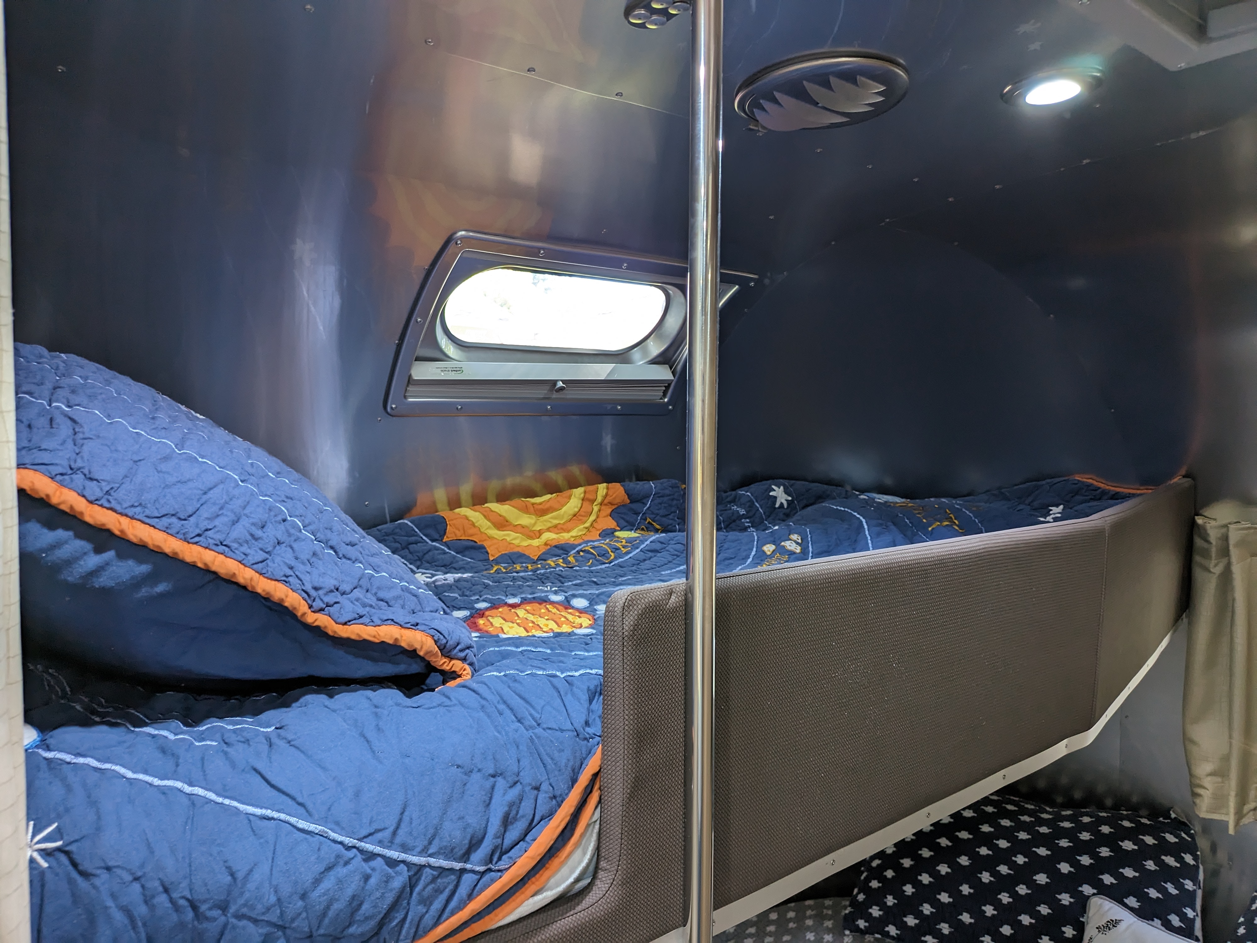Inside an RV rental: view of two aluminum-walled bunk beds with blue bedding, a small window, and overhead lighting.. Airstream Flying Cloud 2020