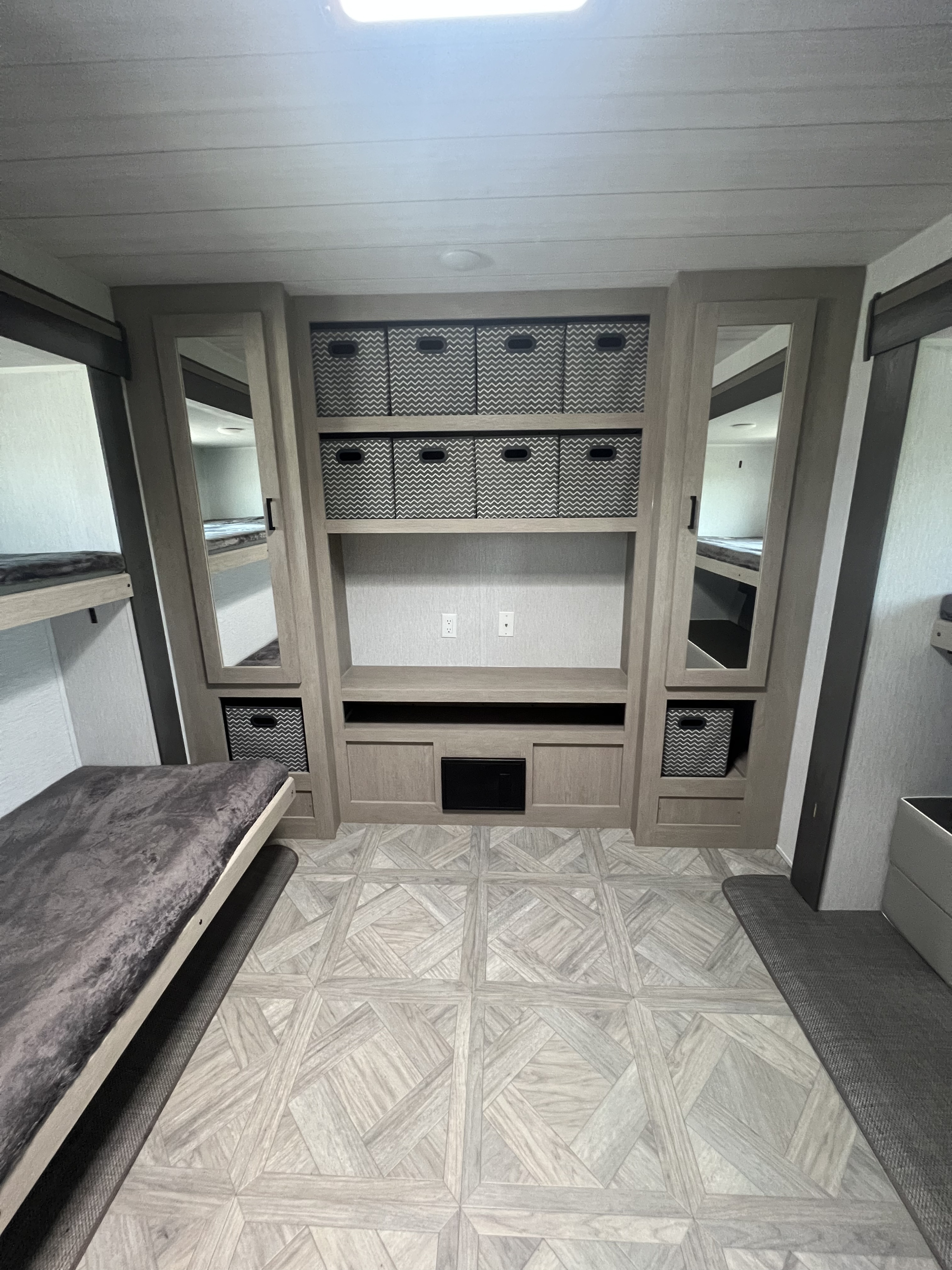 RV rental bunkhouse area with comfortable bunk beds, central storage unit holding woven bins, and patterned floor.. Forest River 31KQBTS 2024