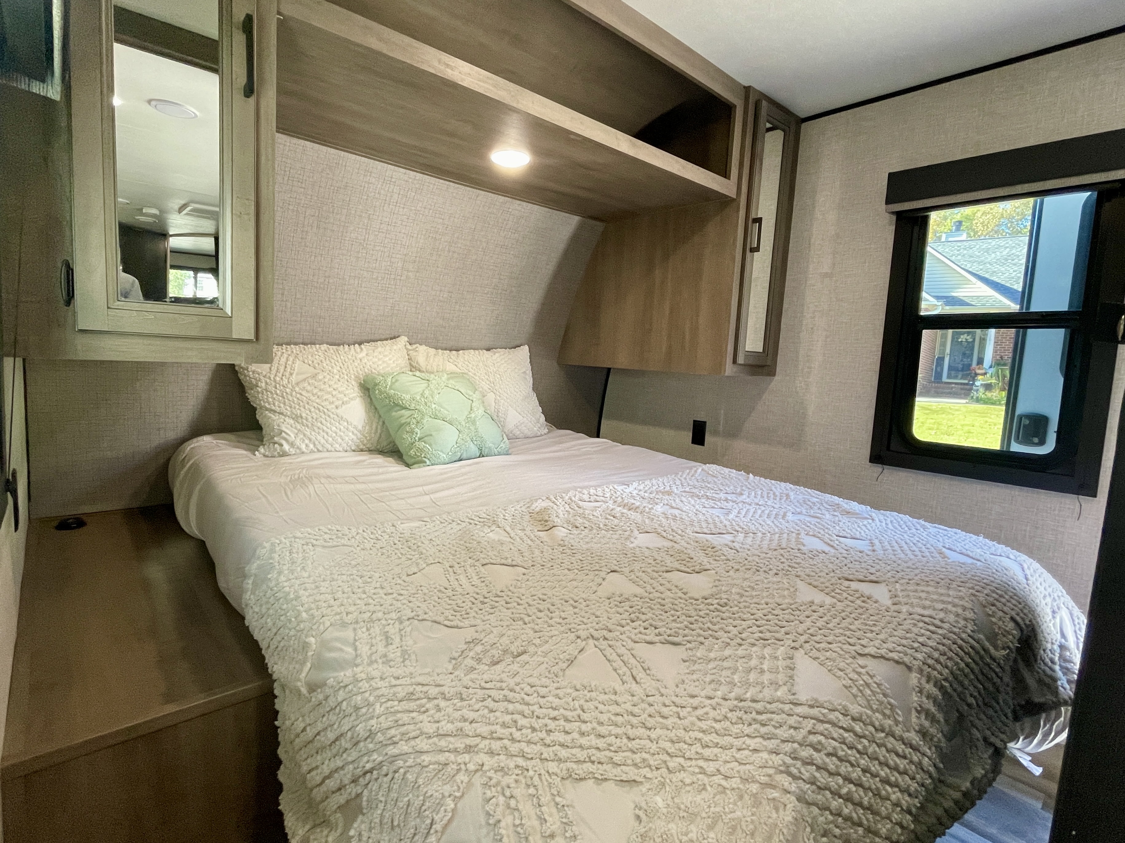 Cozy RV rental bedroom featuring a full bed, overhead storage, and a window overlooking greenery for a comfortable stay.. Starcraft Autumn Ridge 2023