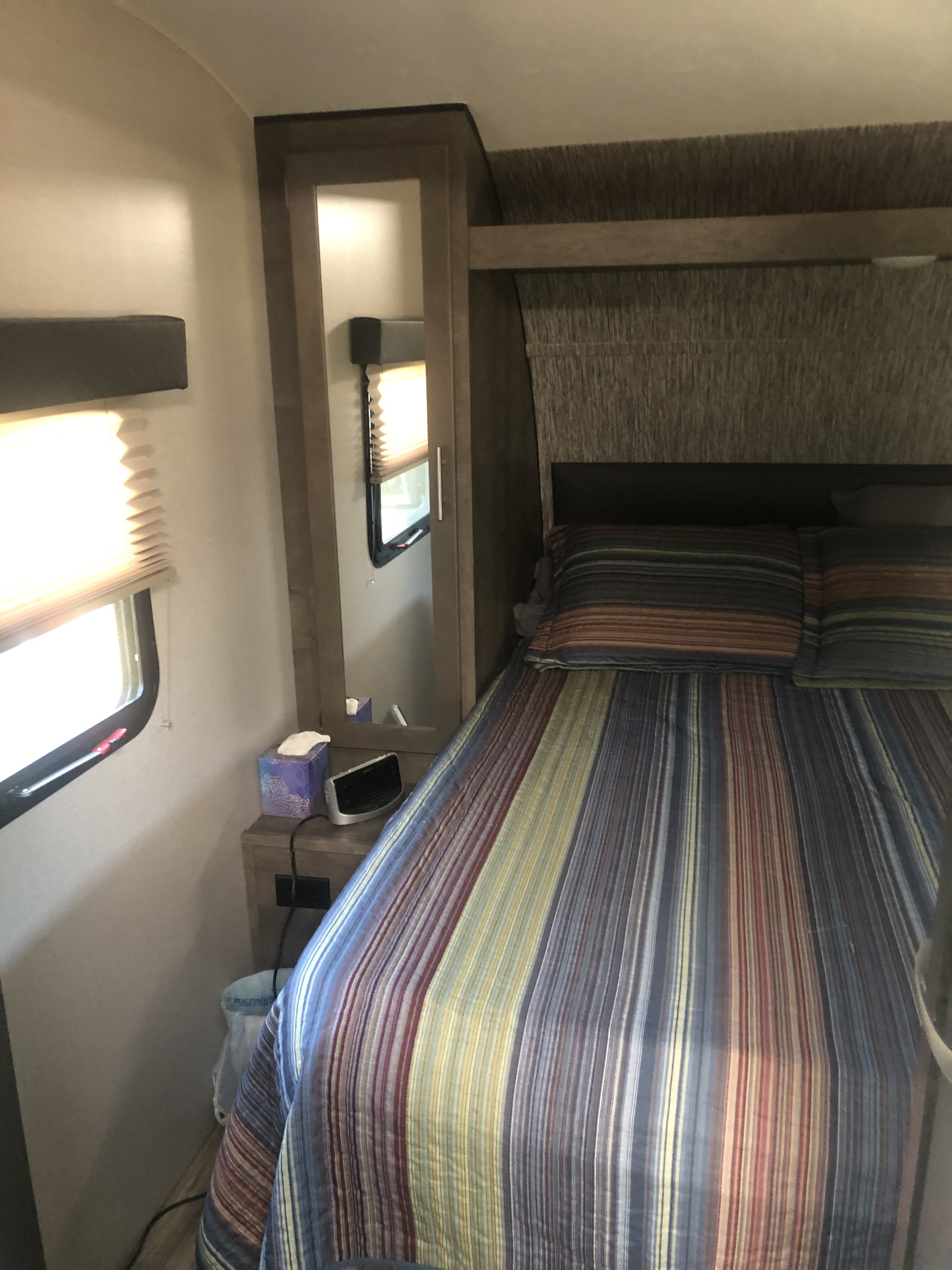 Cozy RV rental bedroom featuring a striped bed, built-in bedside table with mirror, and window.. KZ Connect 2019