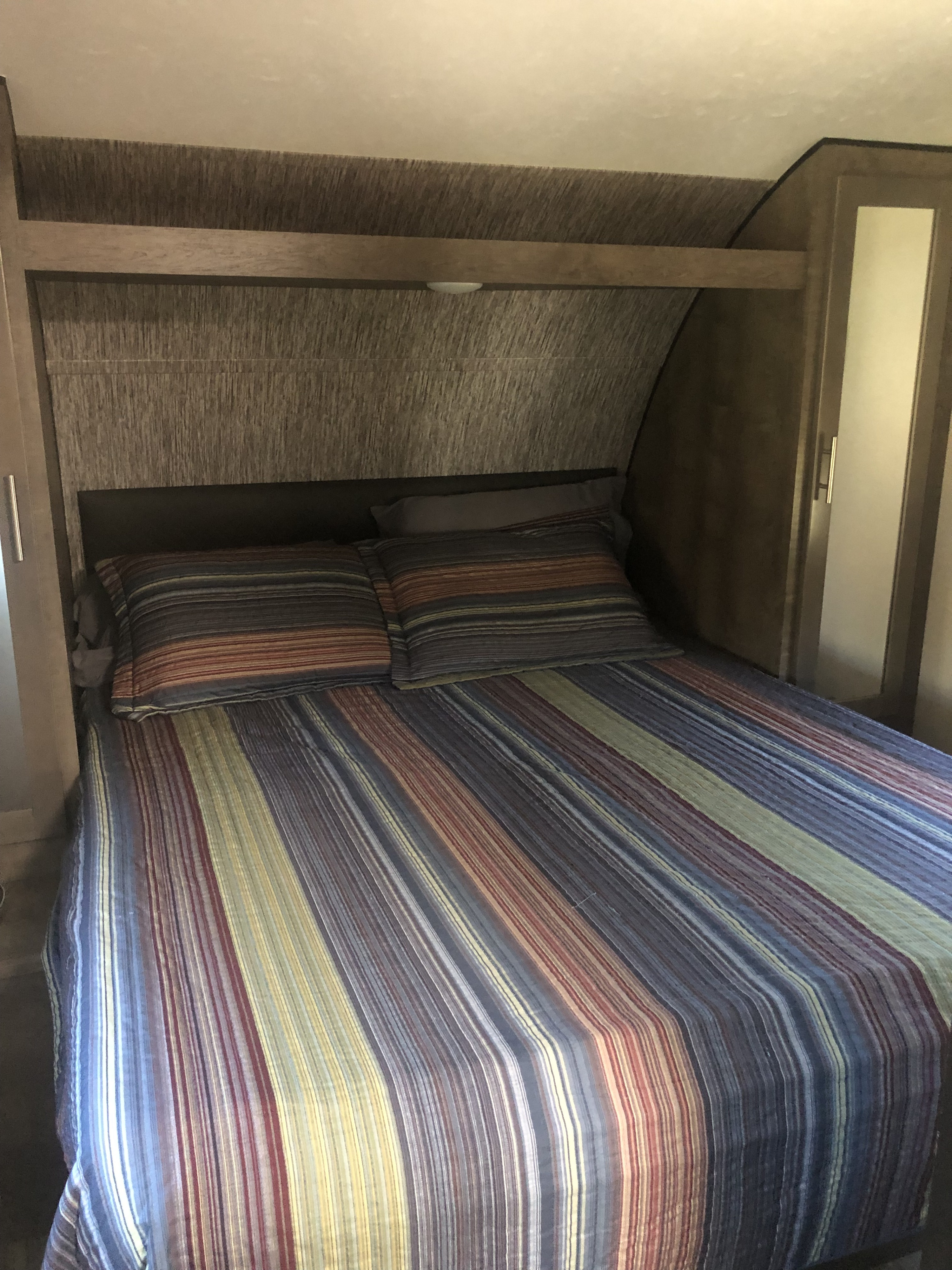Comfortable RV rental bedroom with striped bedding, built-in storage, and mirror. Ideal for your travel needs.. KZ Connect 2019