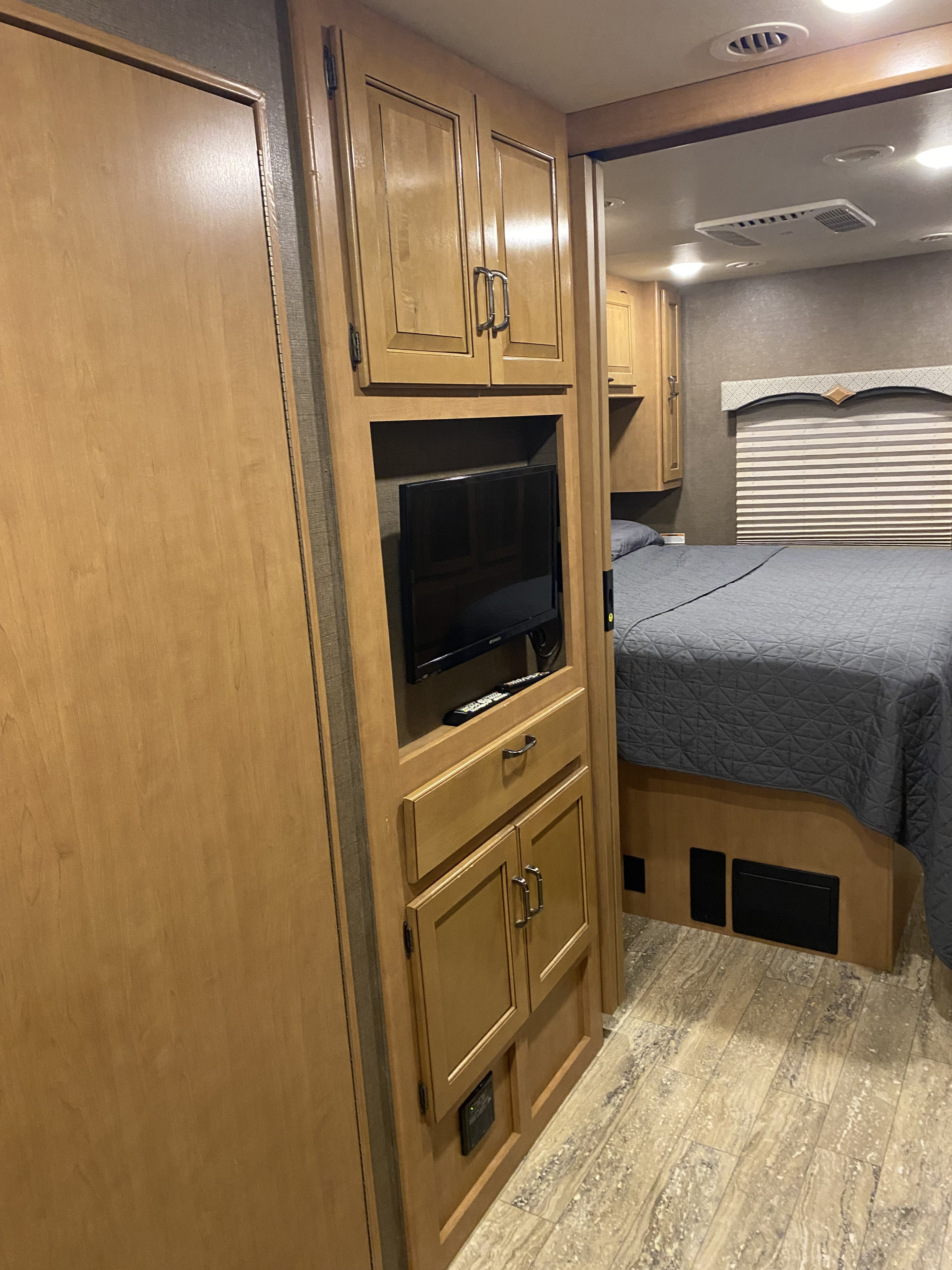RV rental interior: View of bedroom with TV, storage cabinets, and a bed with gray comforter. Wood-look floor visible.. Thor Hurricane 2017
