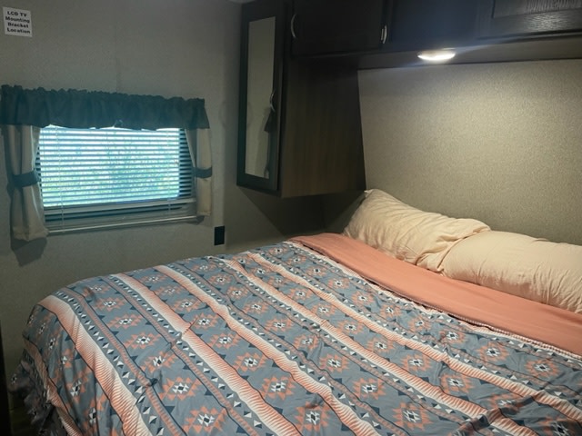 Inside this RV rental bedroom, a patterned bed, window, and wall-mounted light provide comfort.. Keystone RV Springdale 2018