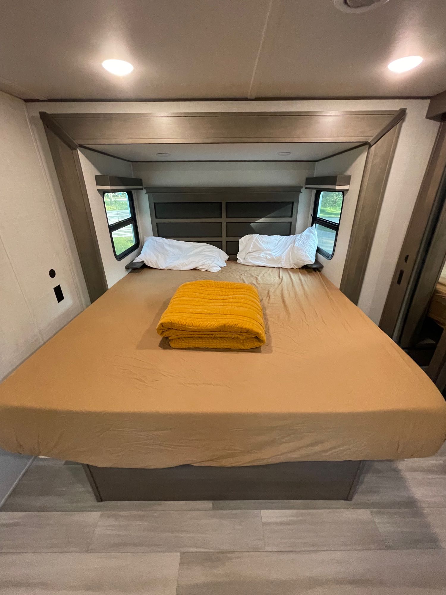 This comfortable RV rental bedroom features a large bed with pillows, a yellow blanket, and windows for a cozy rest.. Grand Design Solitude S-Class 2023
