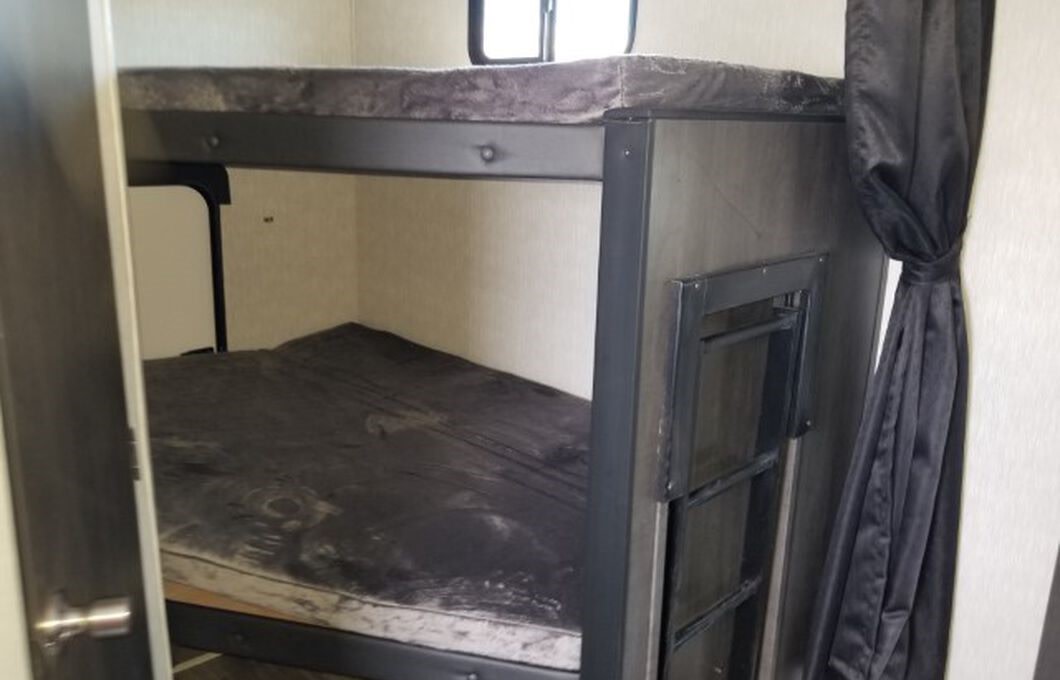 RV rental interior shows sturdy bunk beds with mattresses, a window, ladder, and a black privacy curtain for guests.. Crossroads RV Cruiser Aire 2022