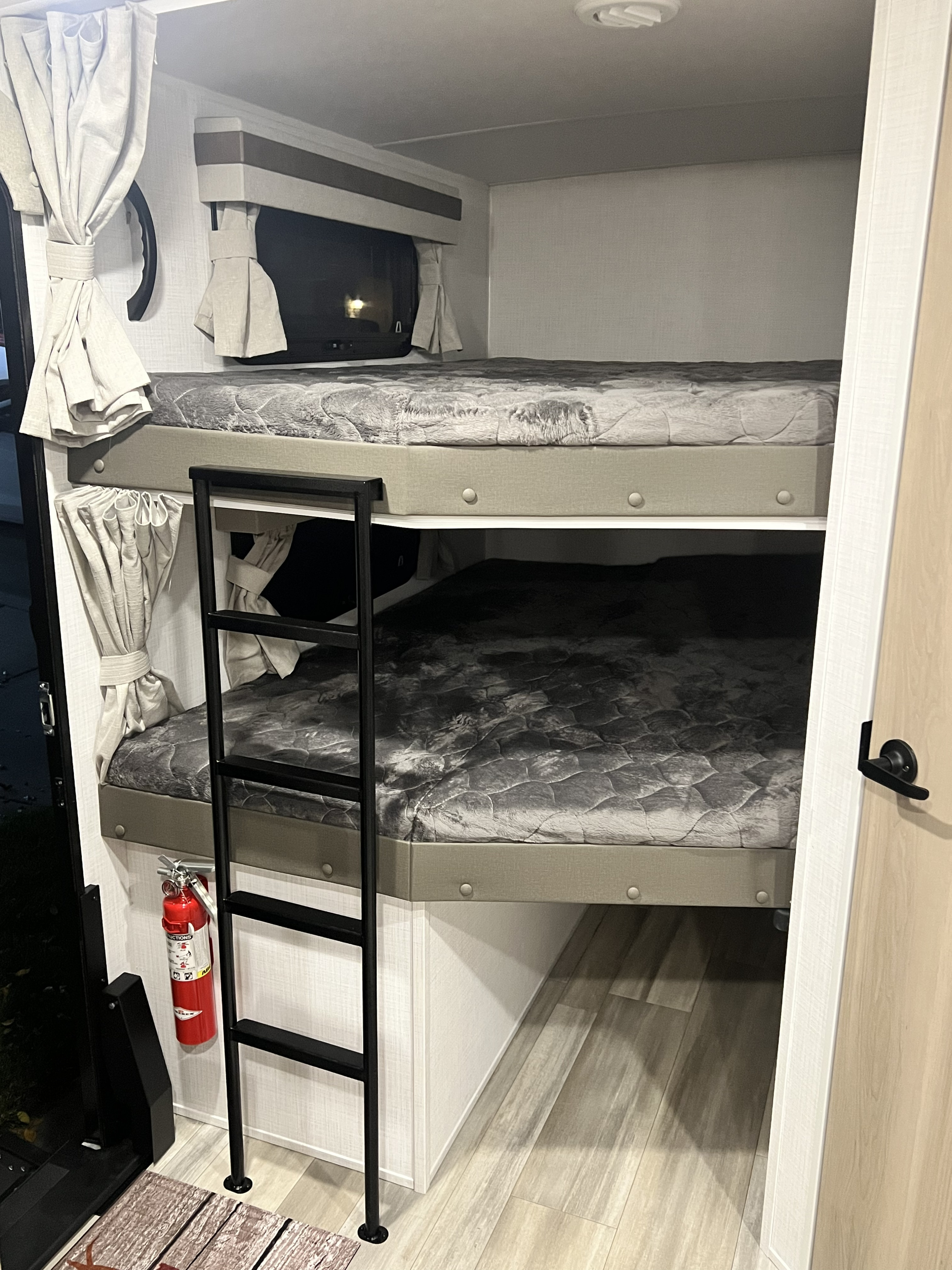 This RV rental interior shows two bunk beds with gray bedding, an access ladder, and a red fire extinguisher on the wall.. Forestriver Rockwood Ulta Lite 2706WS 2024