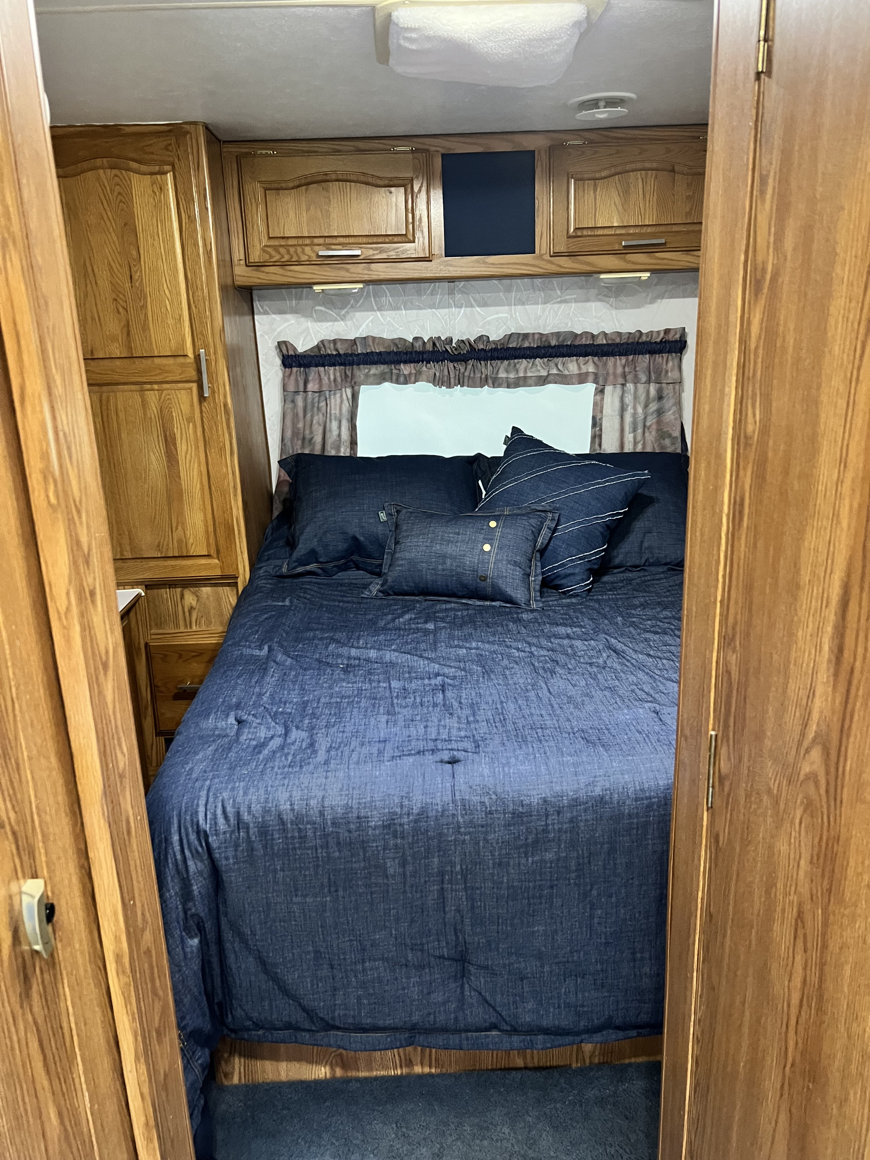 Inside this RV rental bedroom, a cozy bed with blue denim-style bedding is surrounded by warm wood cabinets.. Other Travelmaster 280 1997