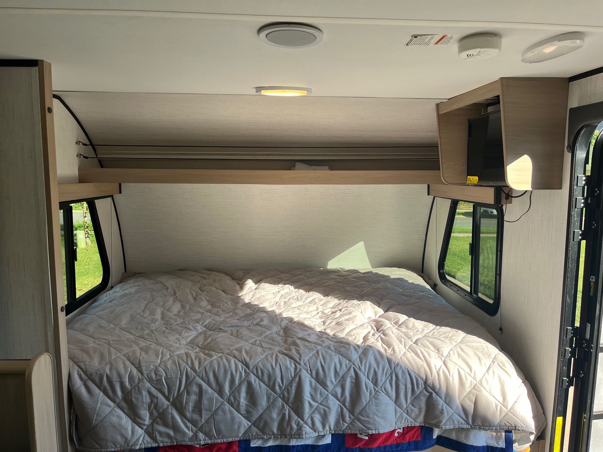 An RV rental bedroom showcasing a quilted bed, sunlight through windows, and a mounted TV. Perfect for travel.. Cruiser RV Hitch 2022