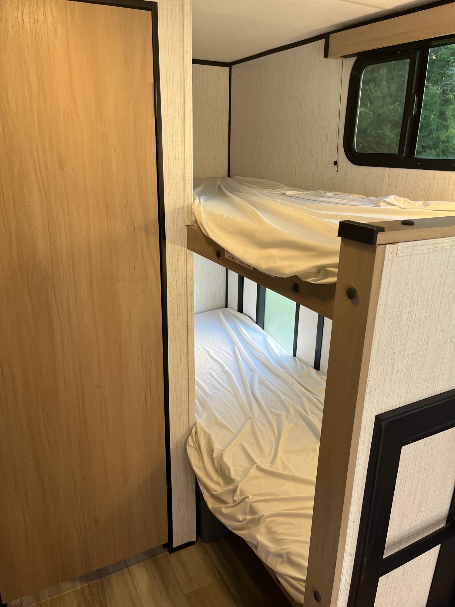 An RV rental's compact interior features tidy bunk beds with white sheets and a wood door nearby.. Cruiser RV Hitch 2022