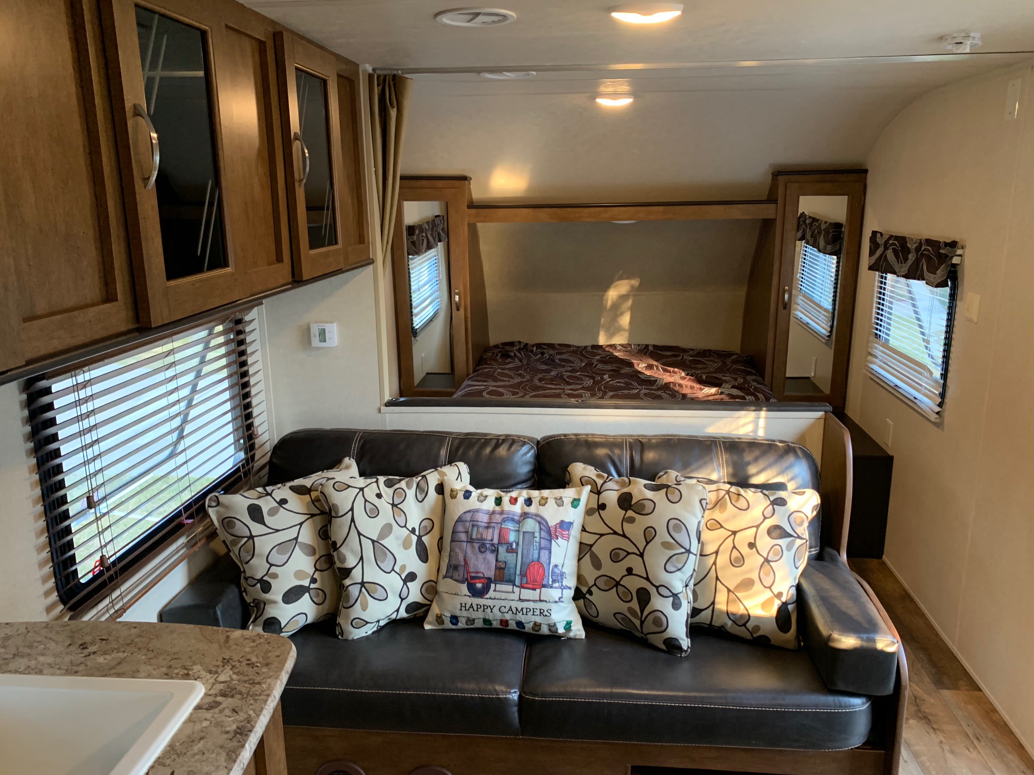 Inside this RV rental: A comfy sofa with throw pillows, a bedroom, kitchen counter, and wooden storage cabinets.. Forest River Salem Cruise Lite 2018