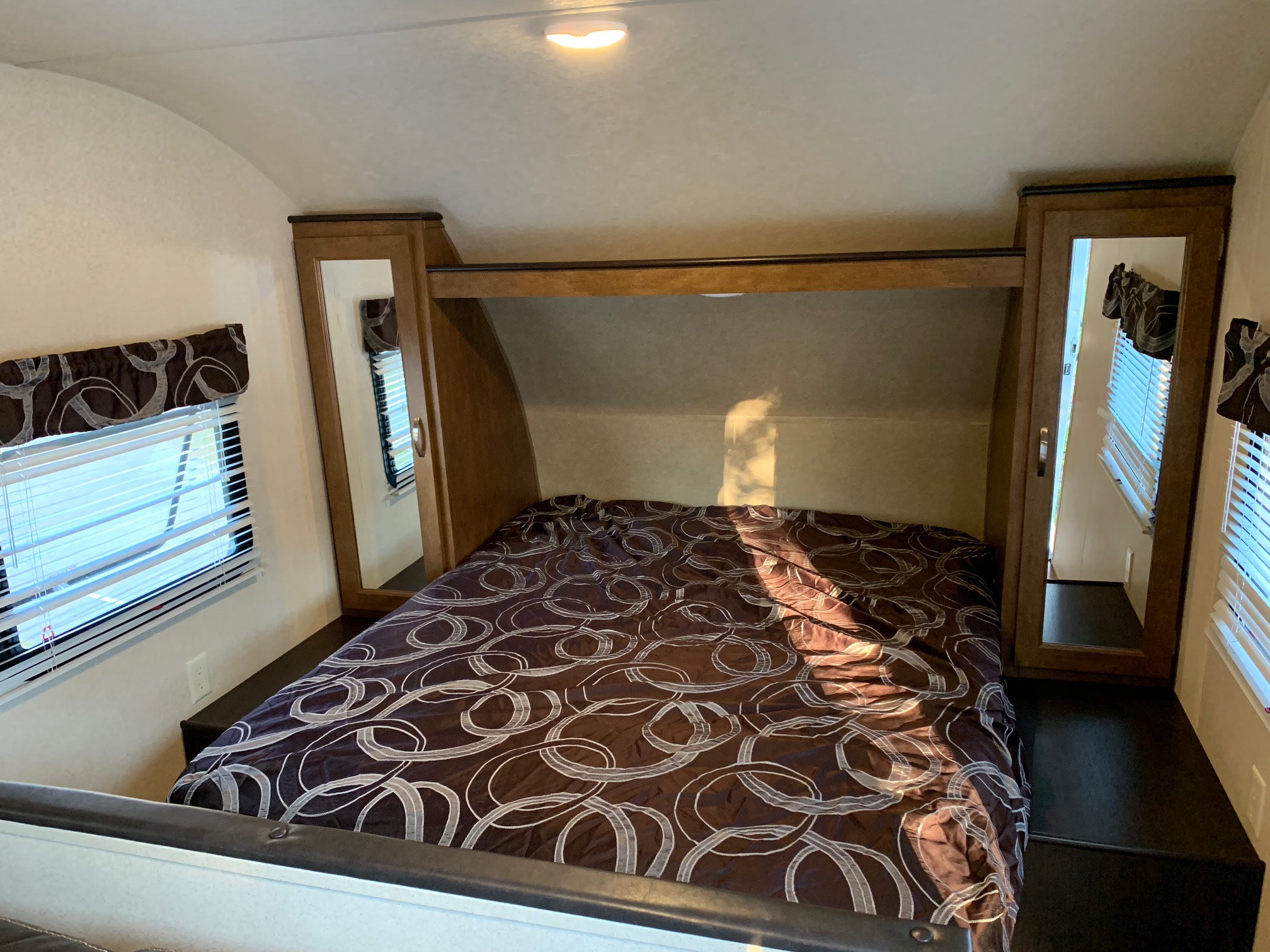 Inside an RV rental: a cozy bedroom with a brown patterned comforter, side cabinets, and windows. Ideal for road trips.. Forest River Salem Cruise Lite 2018