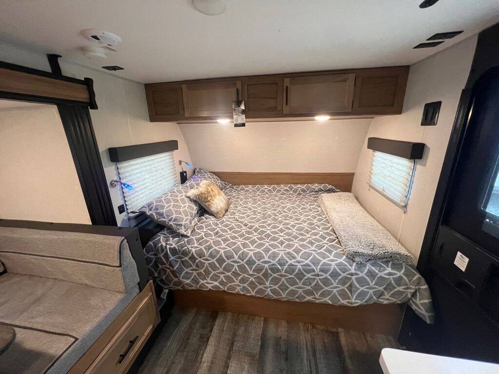 This RV rental interior offers a comfortable bedroom with a large bed, overhead storage, and nearby seating.. Forest River 17JWBL 2024