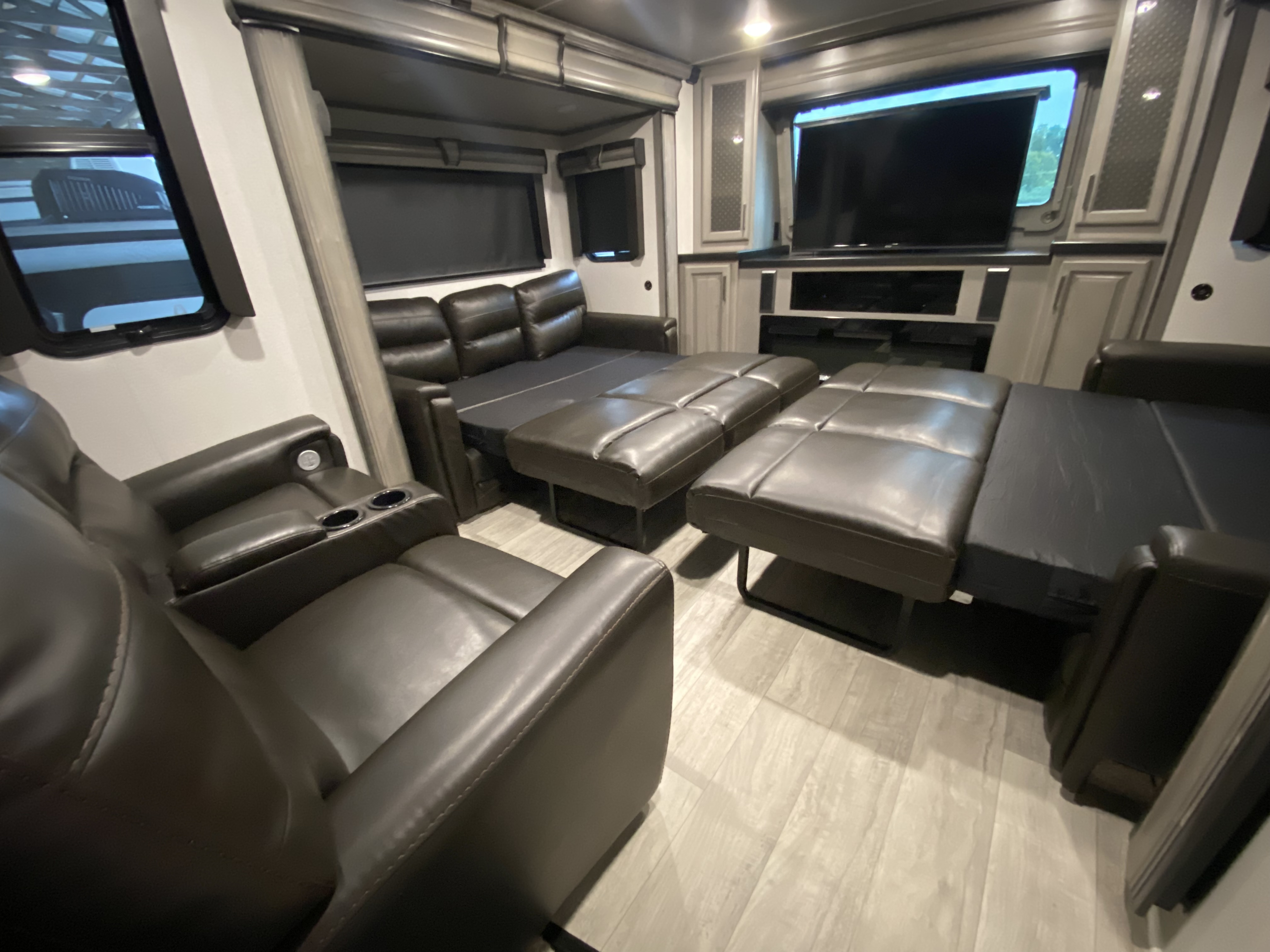 Spacious RV rental living area with dark leather recliners, a pull-out sofa bed, and entertainment center.. Keystone Montana 2023