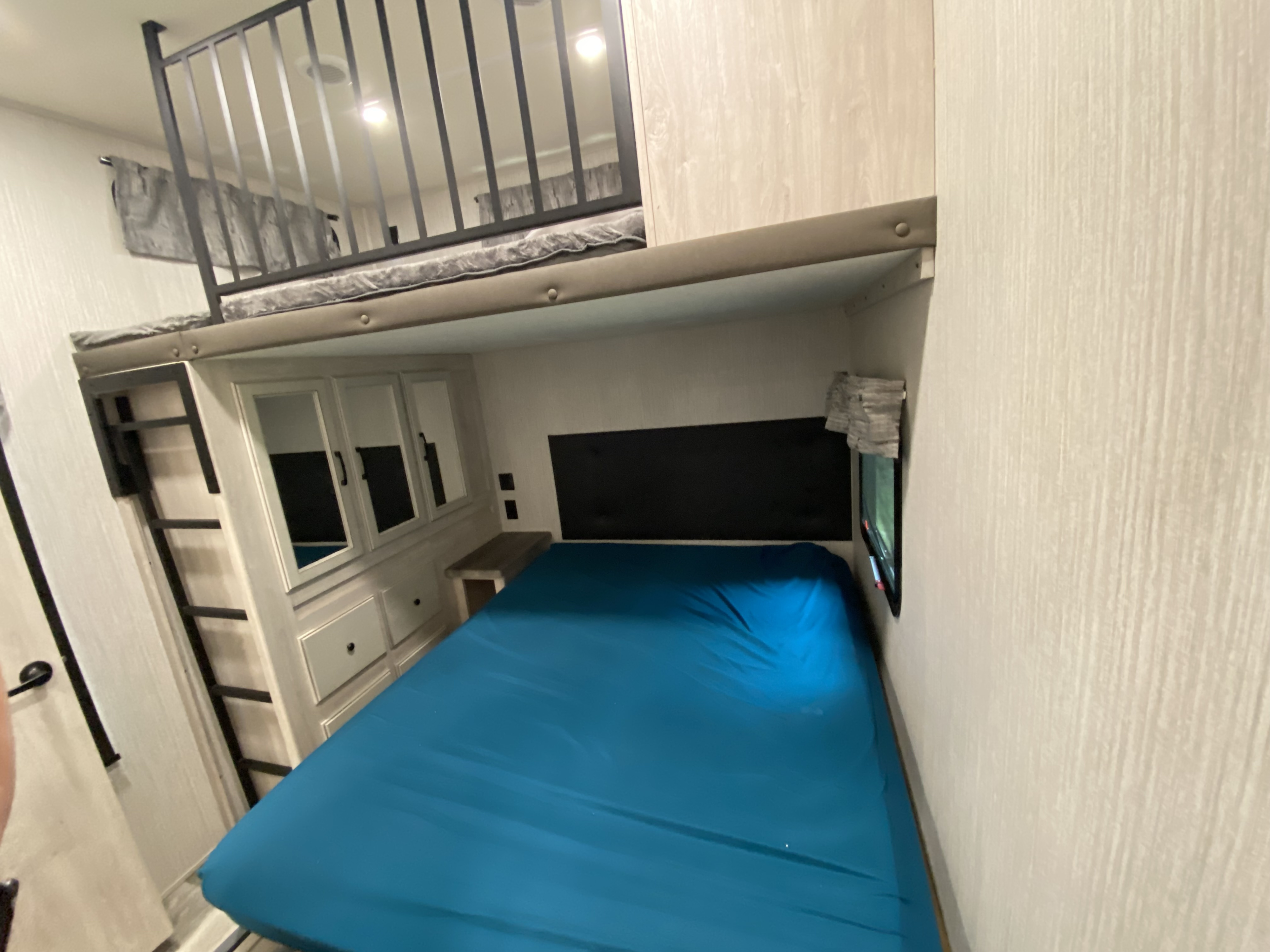 Inside an RV rental: a compact sleeping area featuring a lower bed, an upper loft with safety rails, and storage.. Forest River Sandpiper 2022