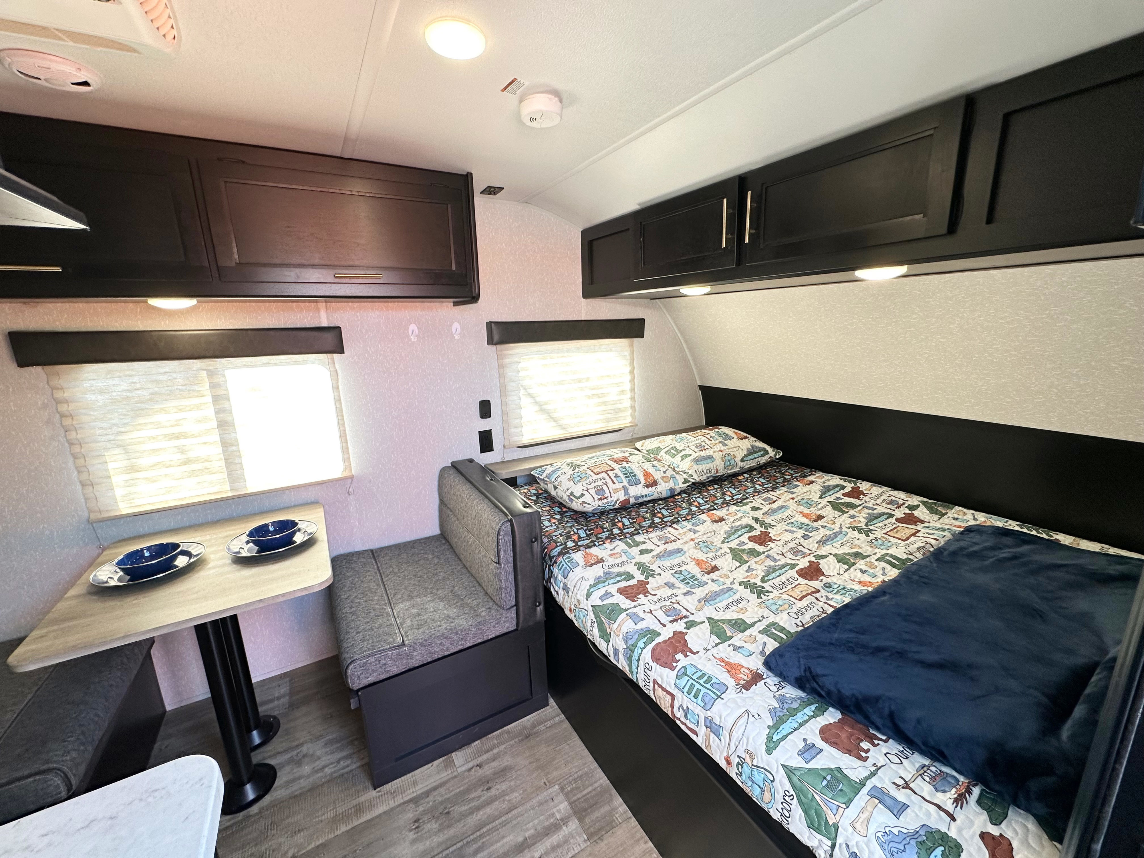 Explore this inviting RV rental interior, featuring a cozy bed with camping quilt, dinette, and overhead storage.. Forest River Cherokee Wolf Pup 2021