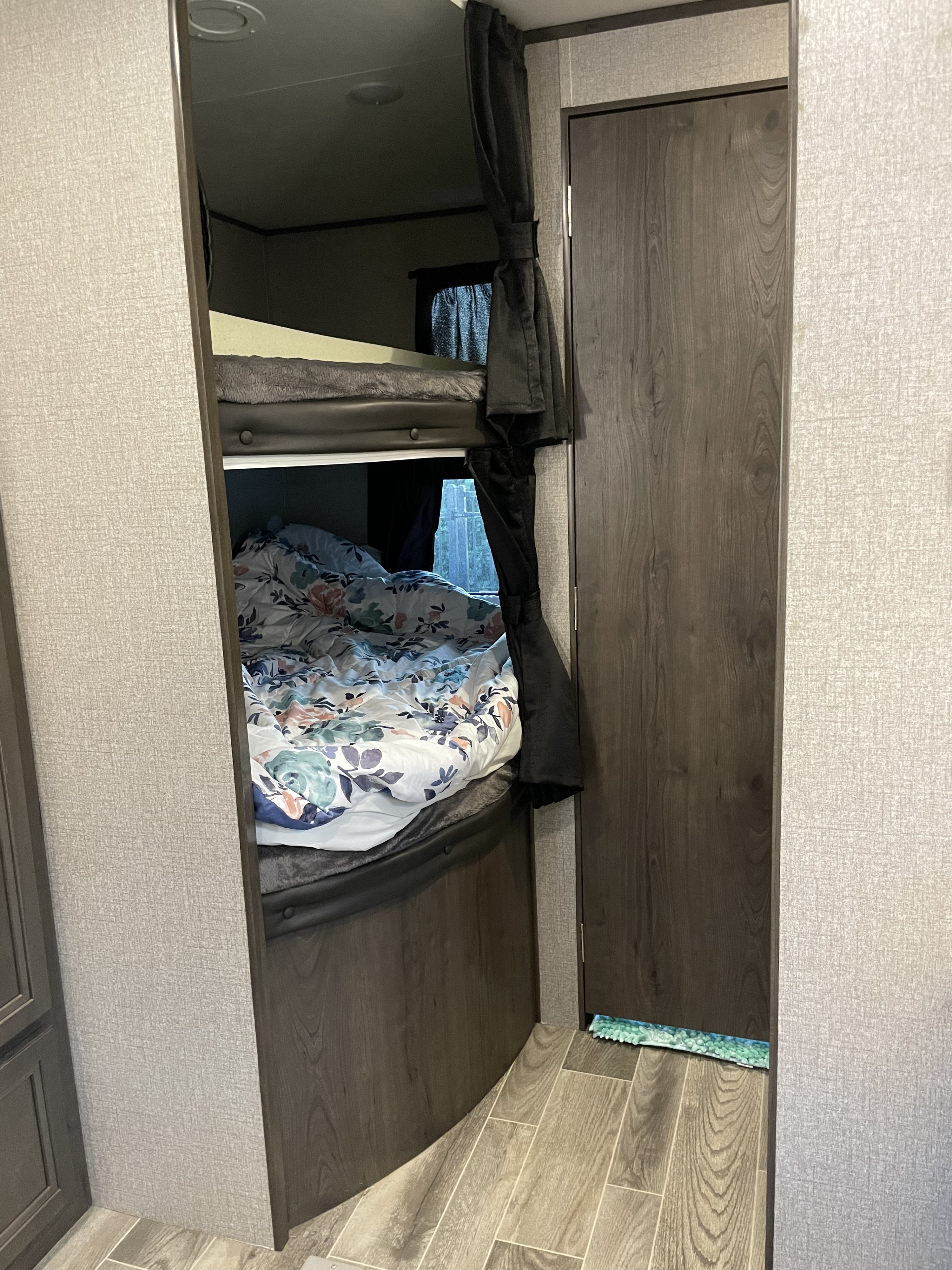 Inside an RV rental: two bunk beds with bedding, dark privacy curtains, and a wooden door.. Jayco Jay Flight 2021