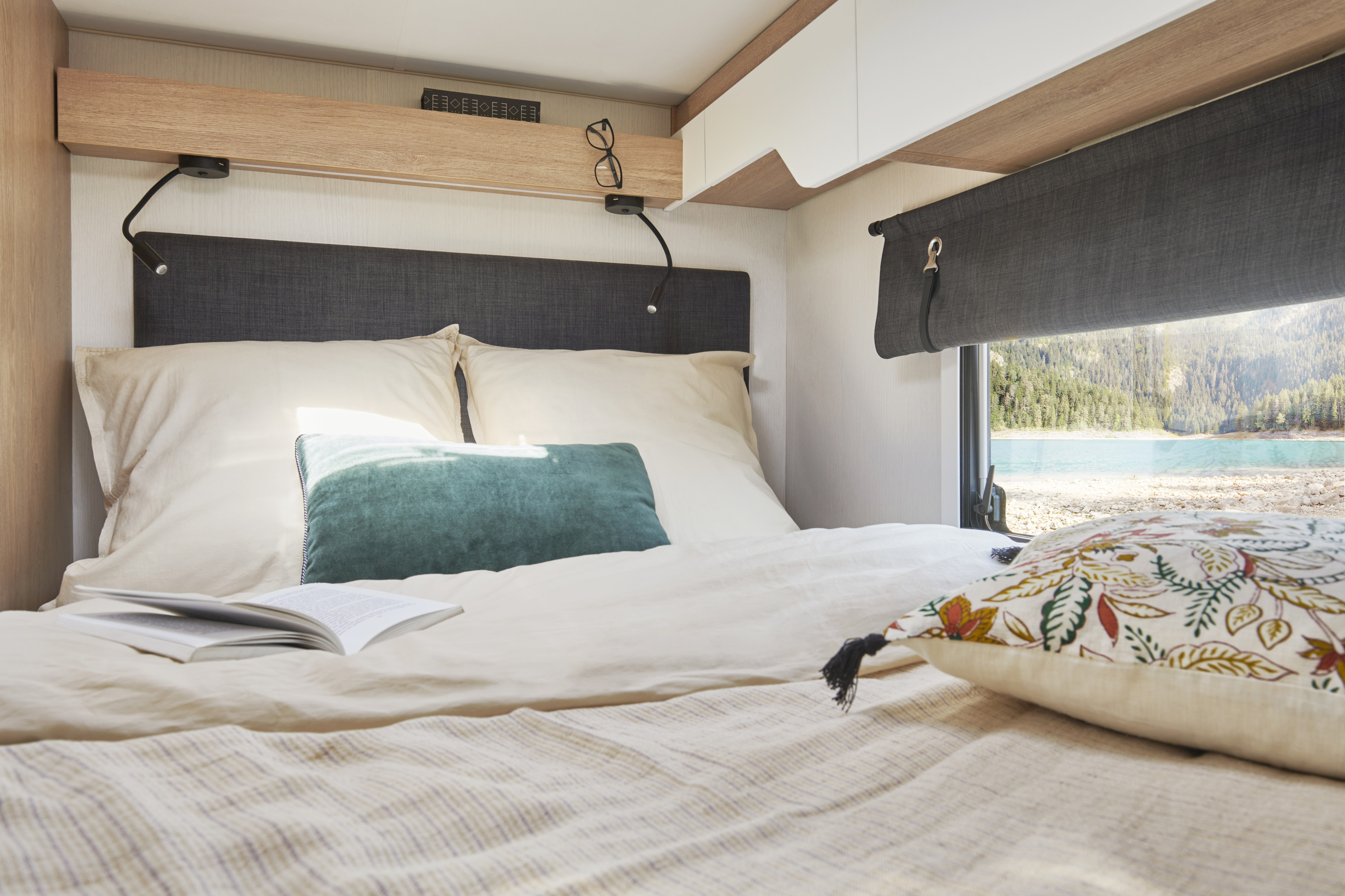 Inside a bright RV rental bedroom with a comfortable bed, reading light, and scenic mountain lake view from the window.. PILOTE A696G Atlas 2025