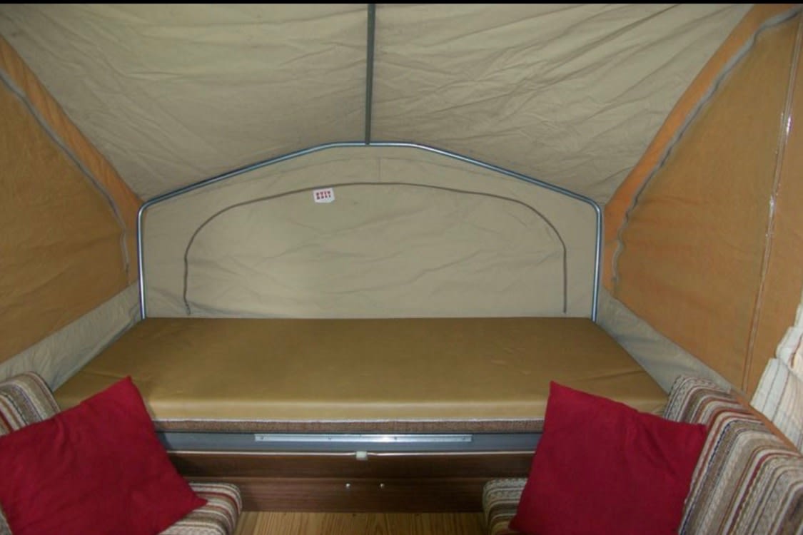 RV rental pop-up camper interior: features a large brown bed, canvas tent, and striped seats with red pillows. Perfect for travel.. Jayco Jay Series 1985