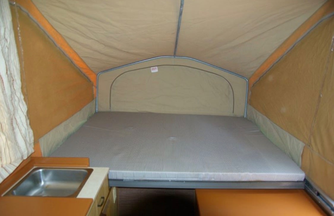 Inside an RV rental pop-up camper: a comfy bed and compact kitchen sink, perfect for camping trips.. Jayco Jay Series 1985