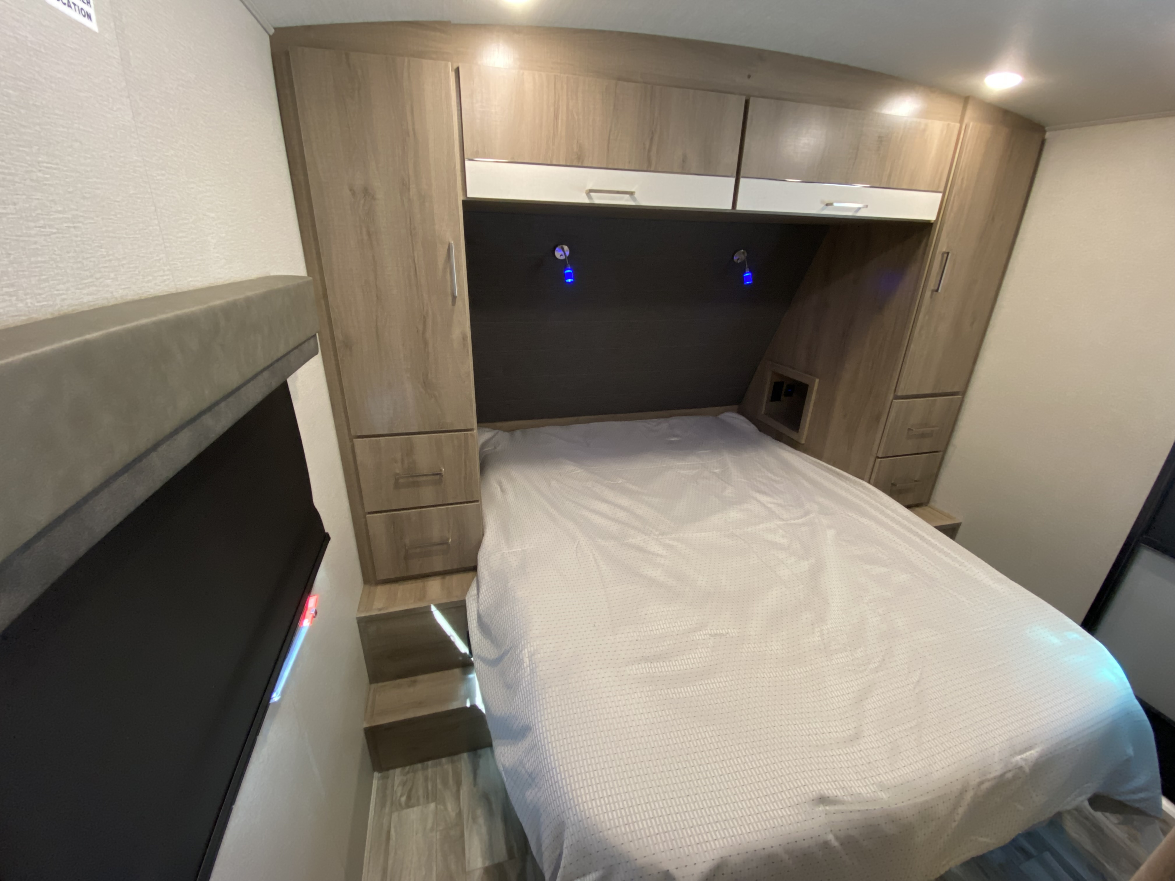 Modern RV rental bedroom with a neatly made bed, wood & white storage cabinets, and ambient blue lights. Cozy travel space.. Grand Design Imagine 2022