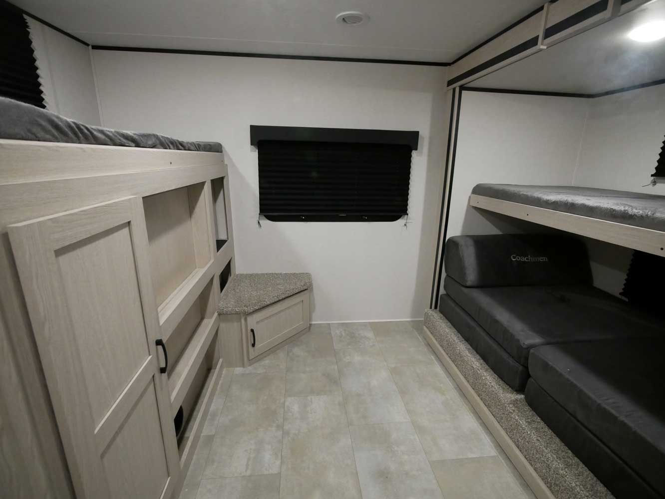 This RV rental interior features light wood bunk beds with integrated storage, a gray folding bed, and a window.. Coachmen Apex 2021