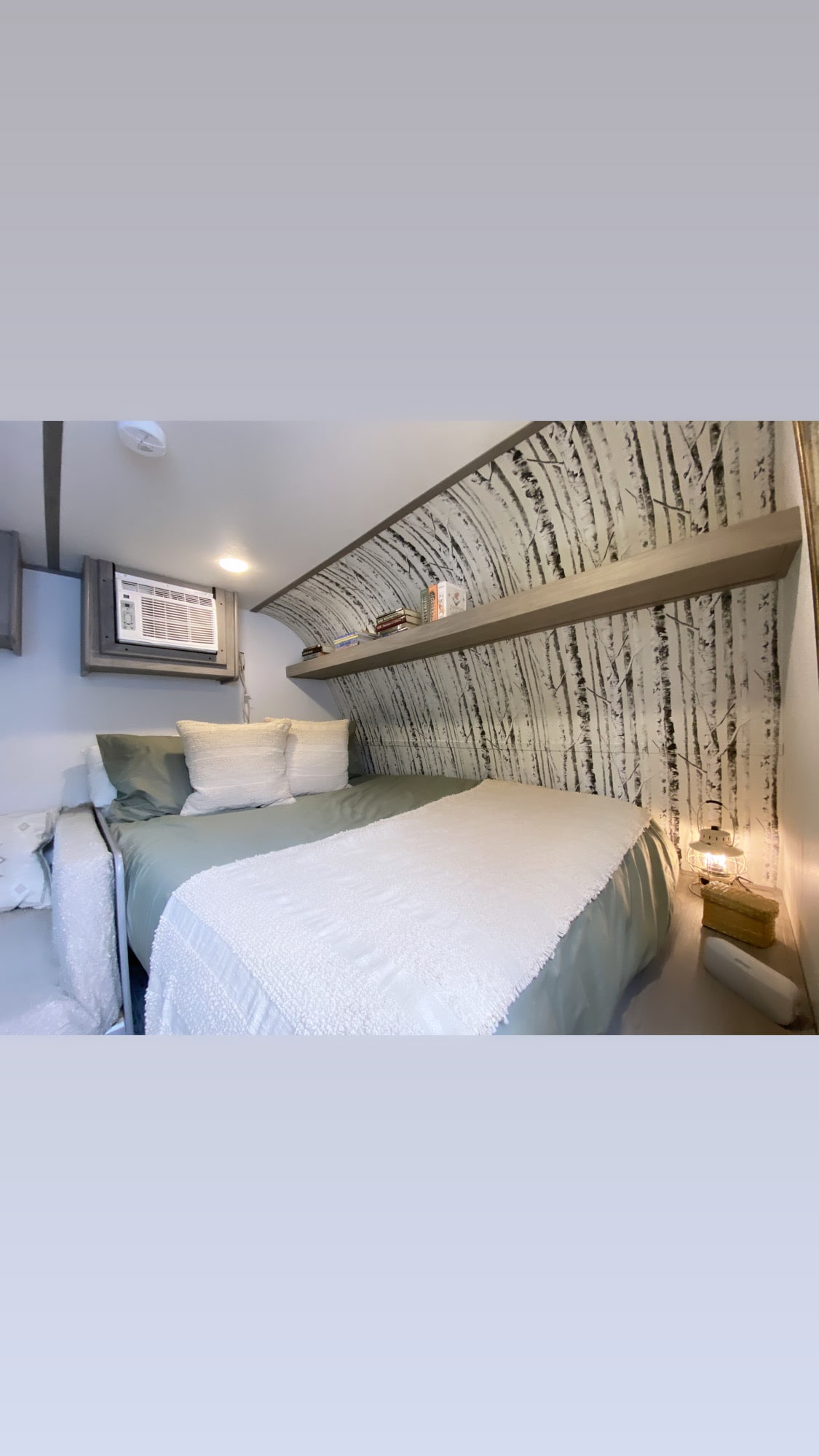 Experience a cozy RV rental bedroom. Features a comfortable bed, birch tree wall, AC unit & built-in shelf for books.. Coleman 17B 2024