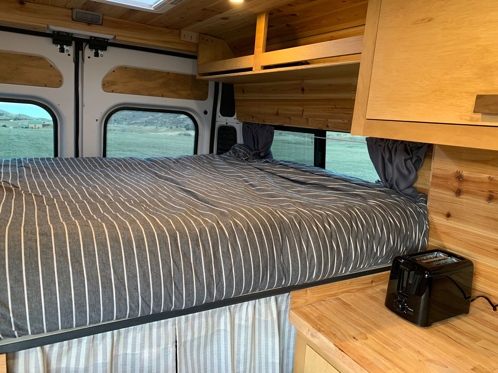 Explore this comfortable RV rental's cozy interior, featuring a striped bed, wooden walls, and a convenient toaster.. RAM Promaster 2500 159wb 2018