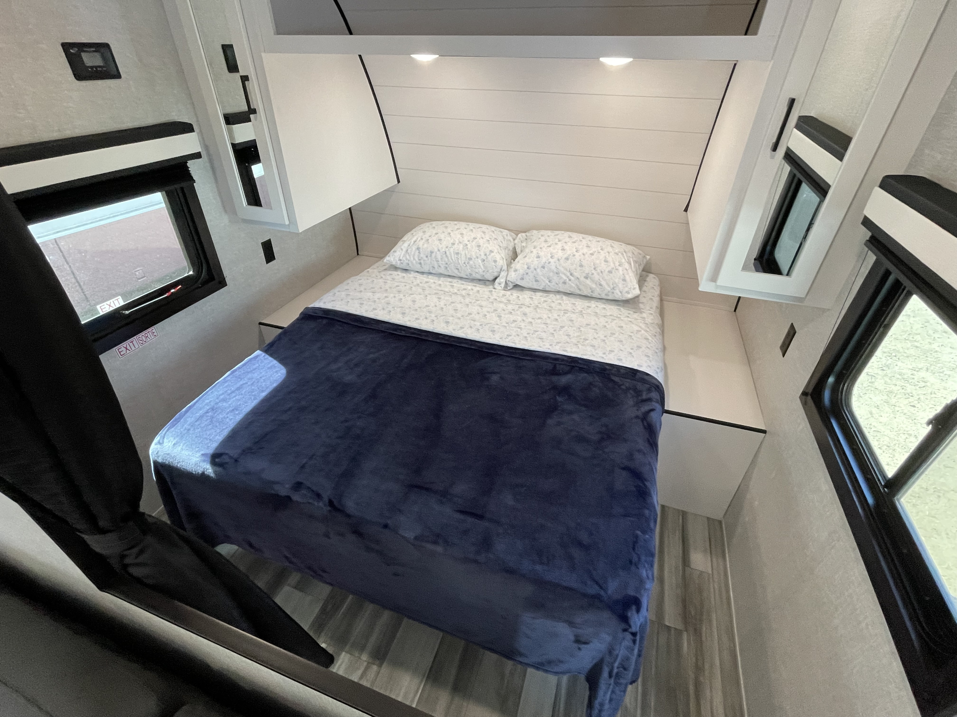 Modern RV rental bedroom. Features a comfy bed with a blue blanket, overhead storage, shiplap wall, and dual windows.. Jayco Jay Flight 2024