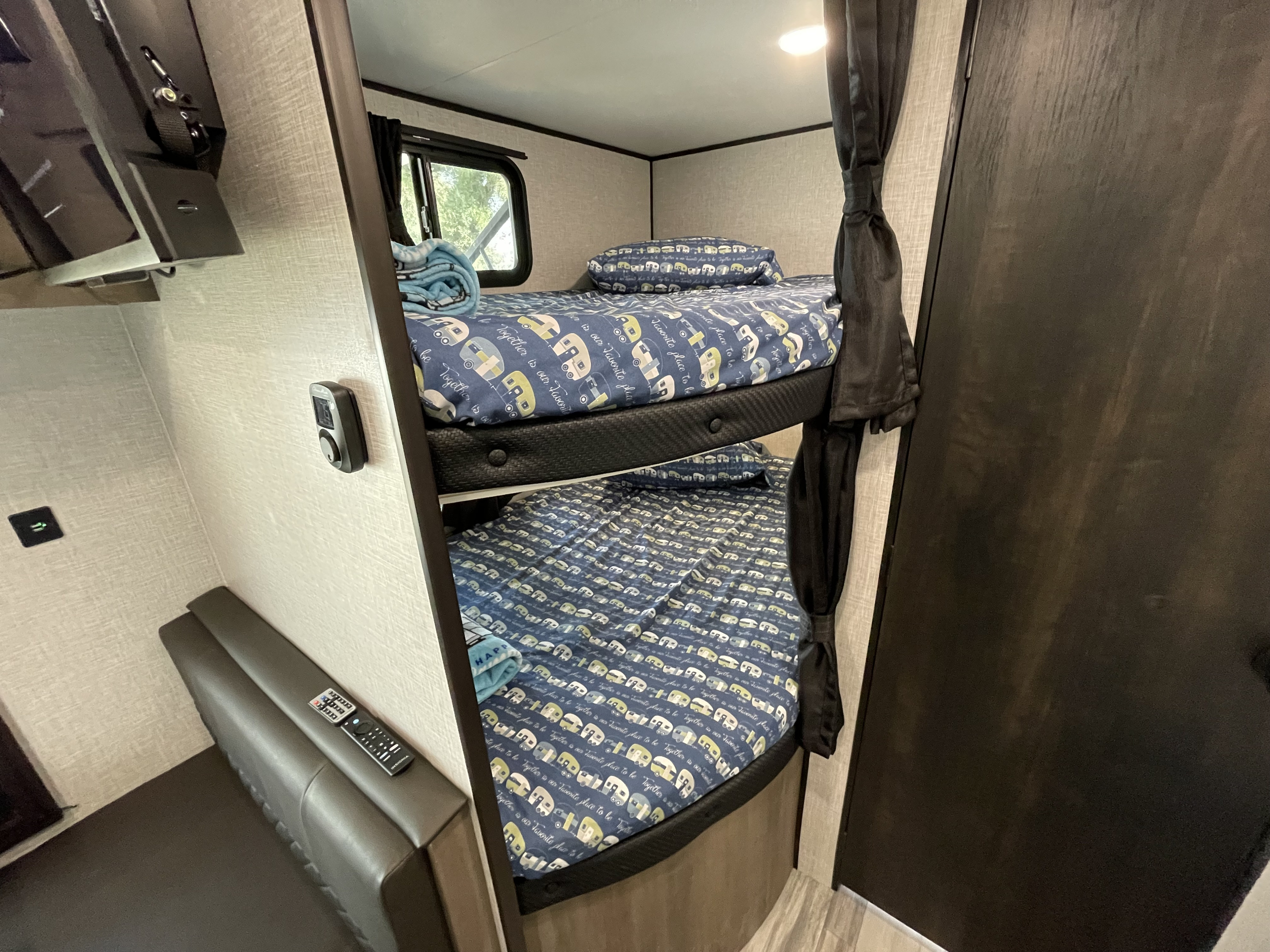 Cozy RV rental bunk beds with fun camper-themed bedding, ideal for family adventures. Features include a TV and seating.. Jayco Jay Flight 2024