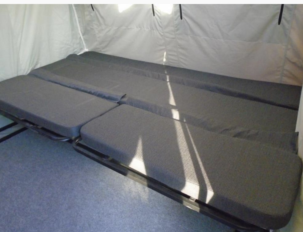 Inside an RV rental, a flexible dark gray cushioned bed/seating area on a metal frame is set against light fabric walls.. Custom Other 2019