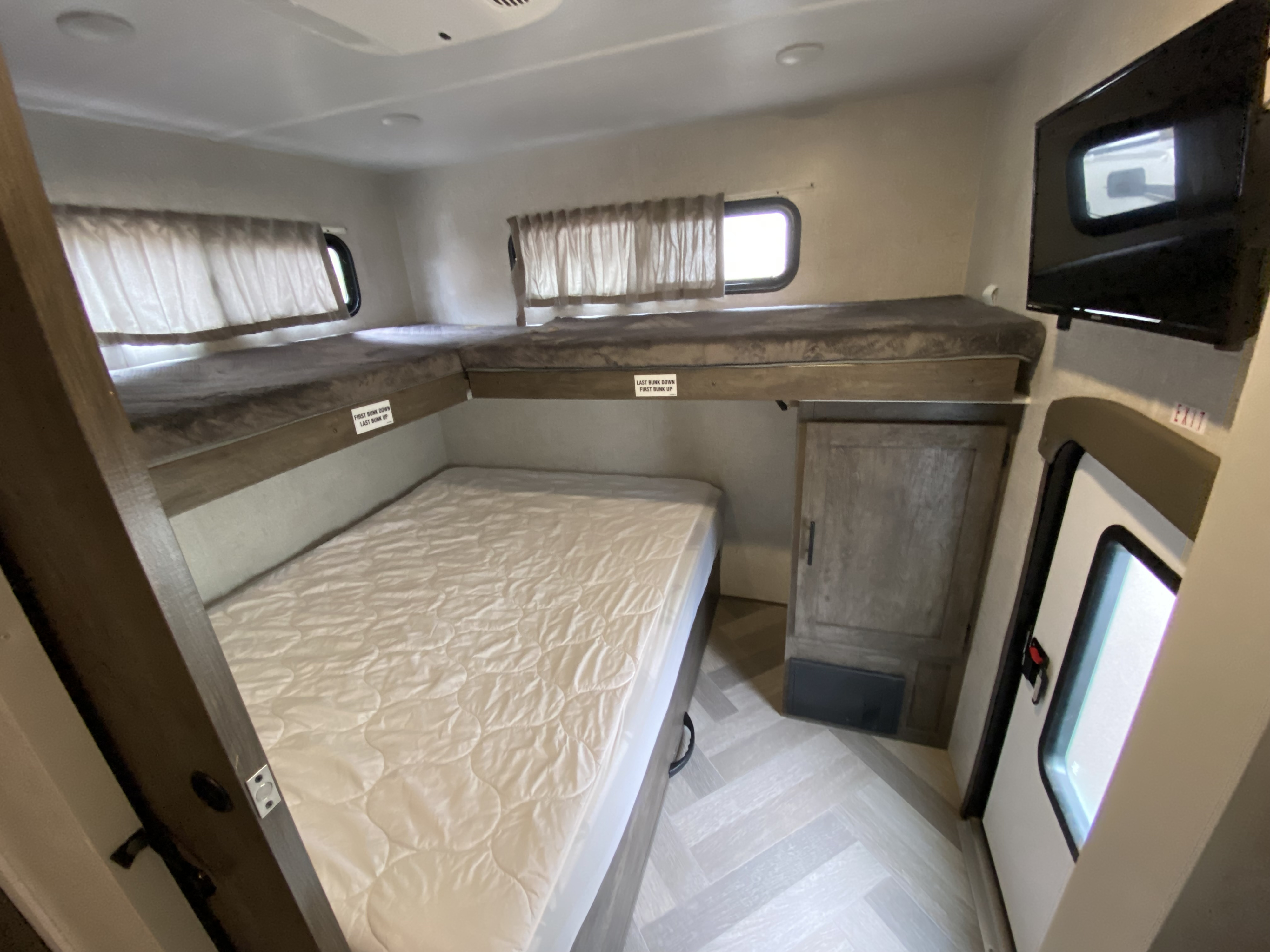 Cozy RV rental bedroom with a large lower bed, two bunk beds above, TV, & exit door. Sleep in comfort on your next adventure.. Forest River Salem 2021