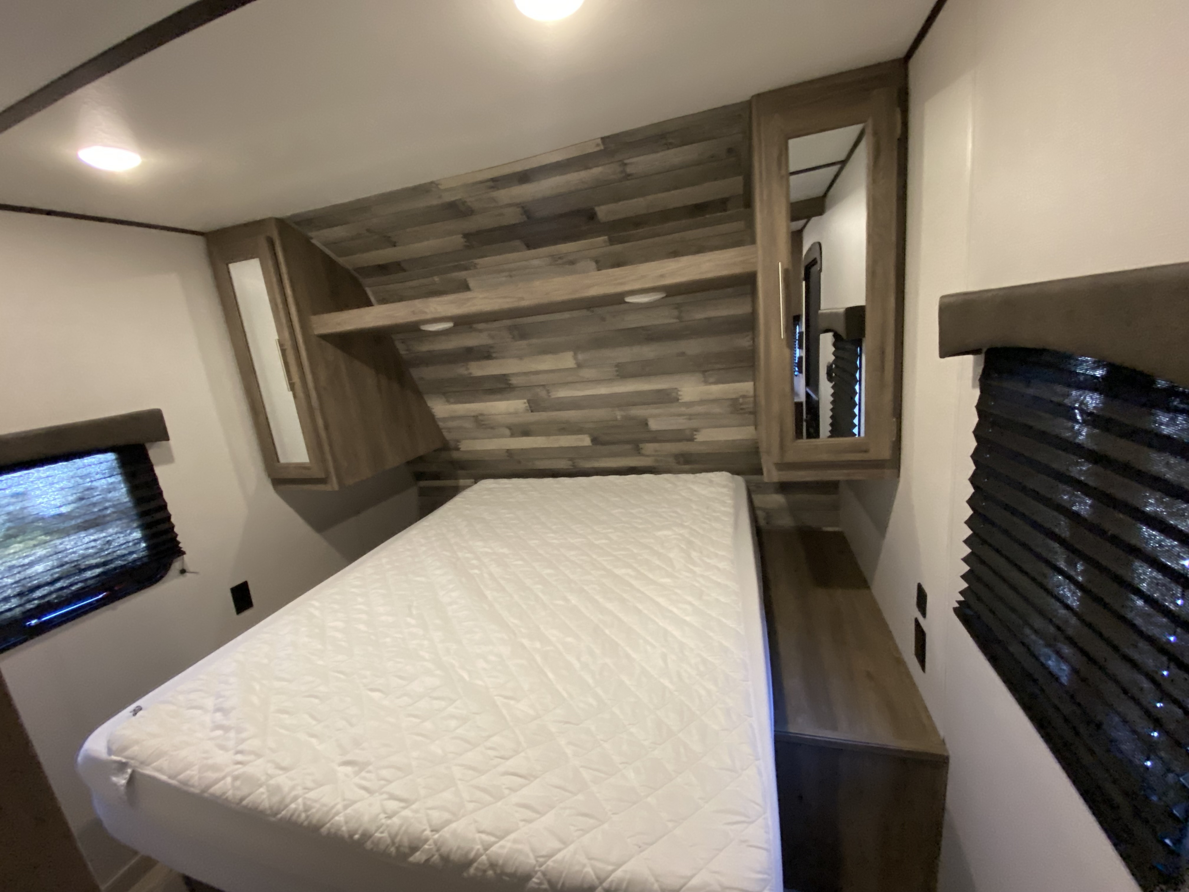 Bright RV rental bedroom features a comfy bed, stylish wood accents, mirrored cabinets, and windows with blinds.. Keystone Crossroads Zinger 2021