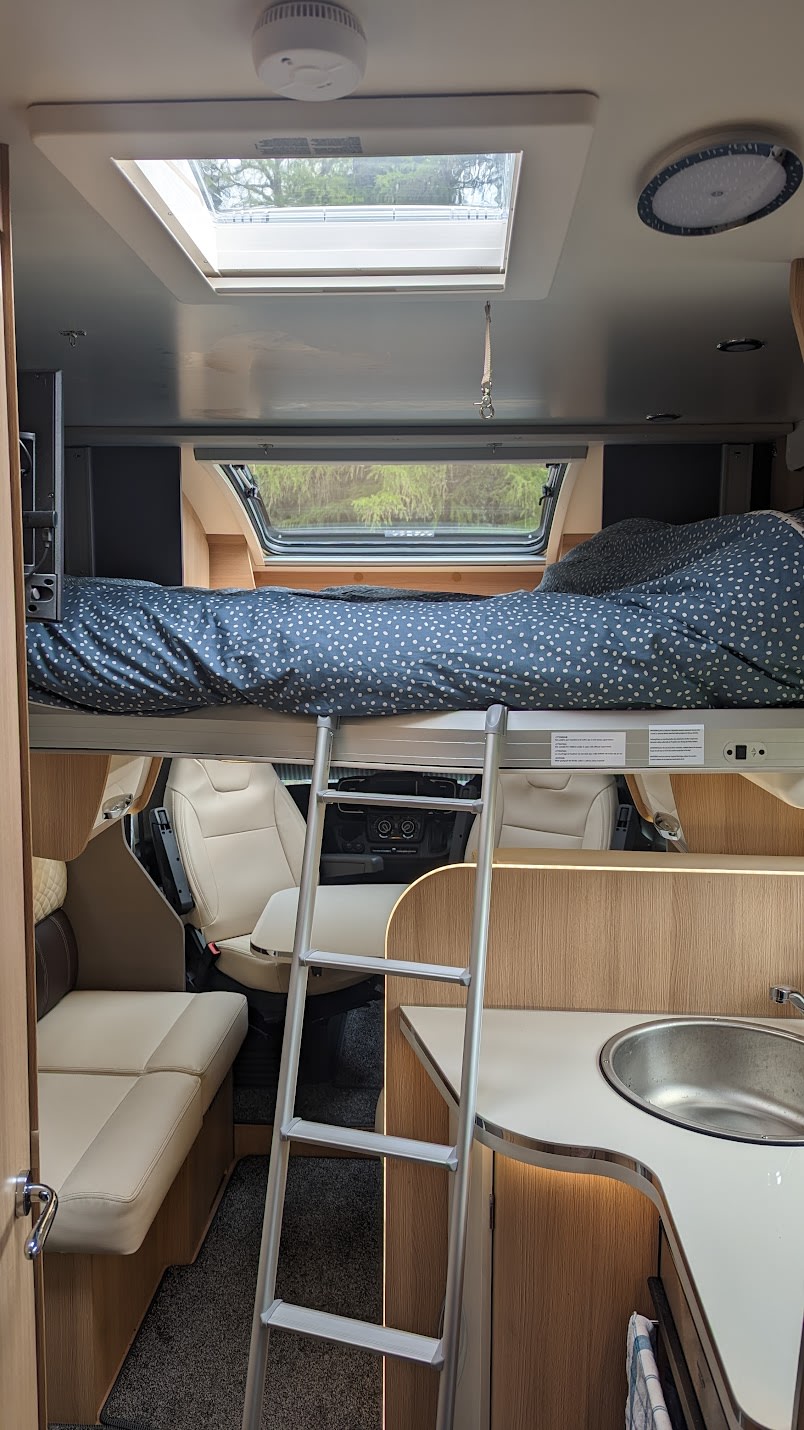 This RV rental interior features a bunk bed with ladder, kitchen, dinette, and front cabin seats below. A skylight is overhead.. McLouis Fusion 360 2023