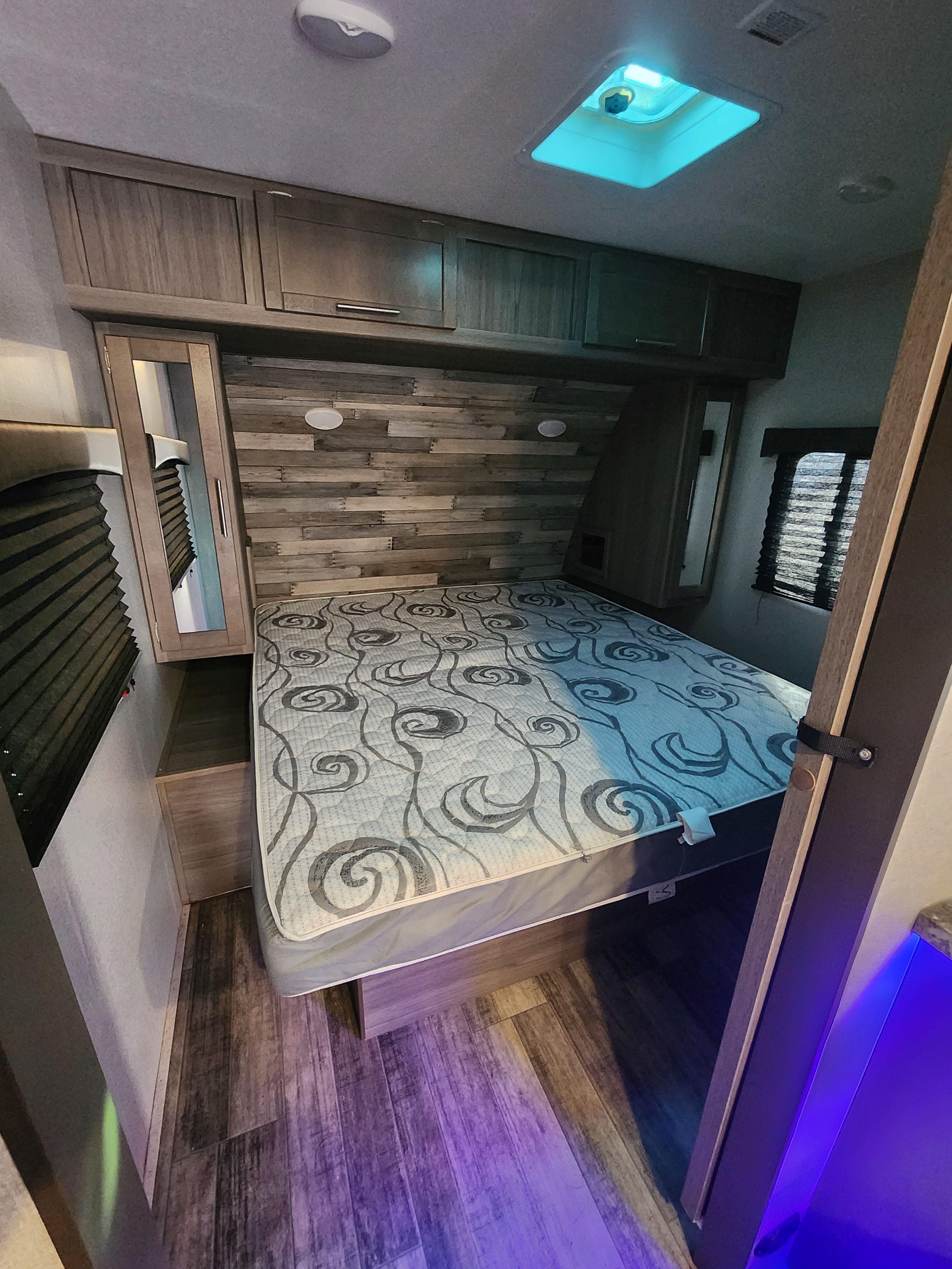 Cozy RV rental bedroom features a patterned bed, wood-look accent wall, overhead storage, and ceiling vent with blue light.. Crossroads Volante 2020