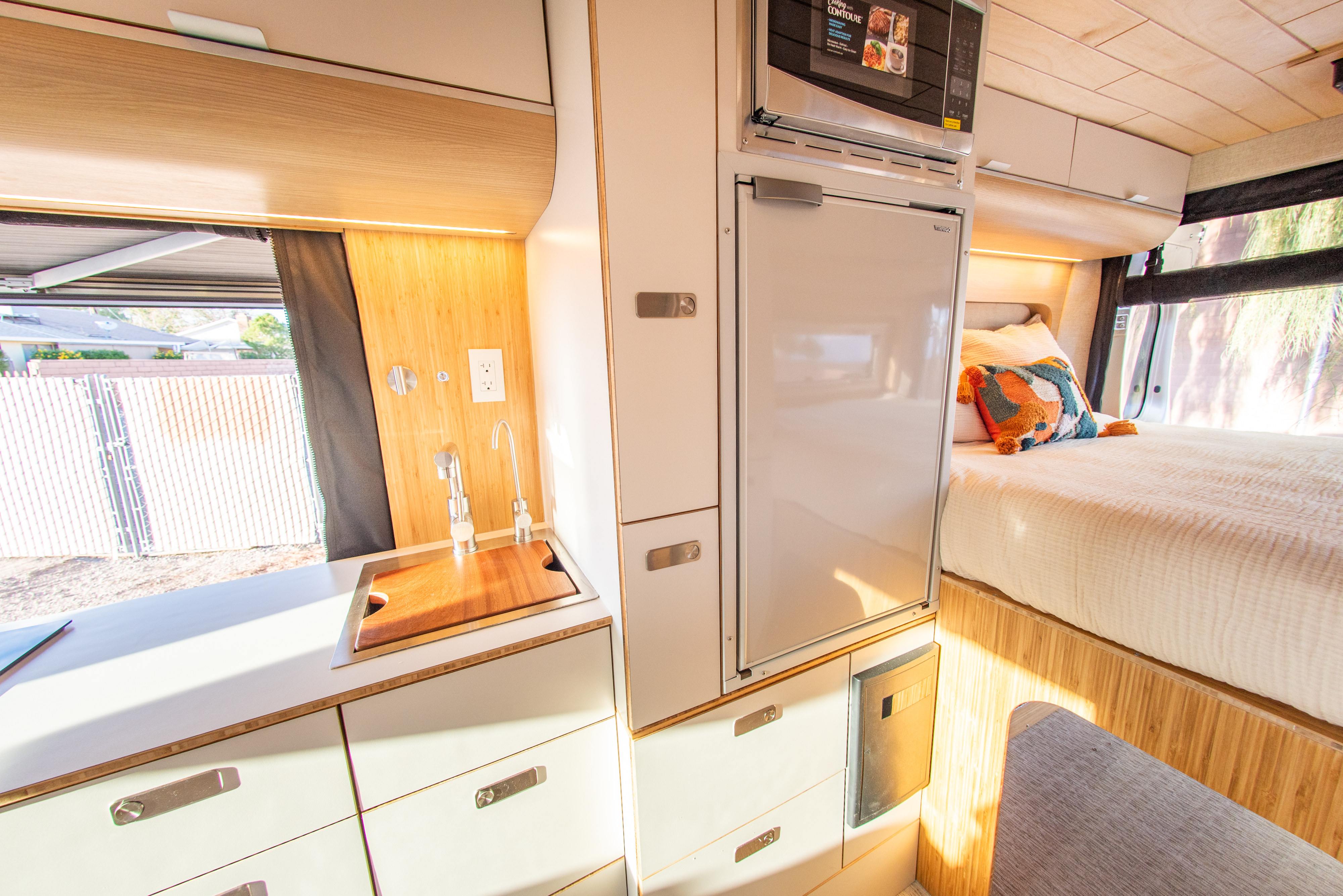 Bright RV rental interior: integrated kitchen with sink, microwave, fridge, and a comfortable bed.. Noovo Lite 2023
