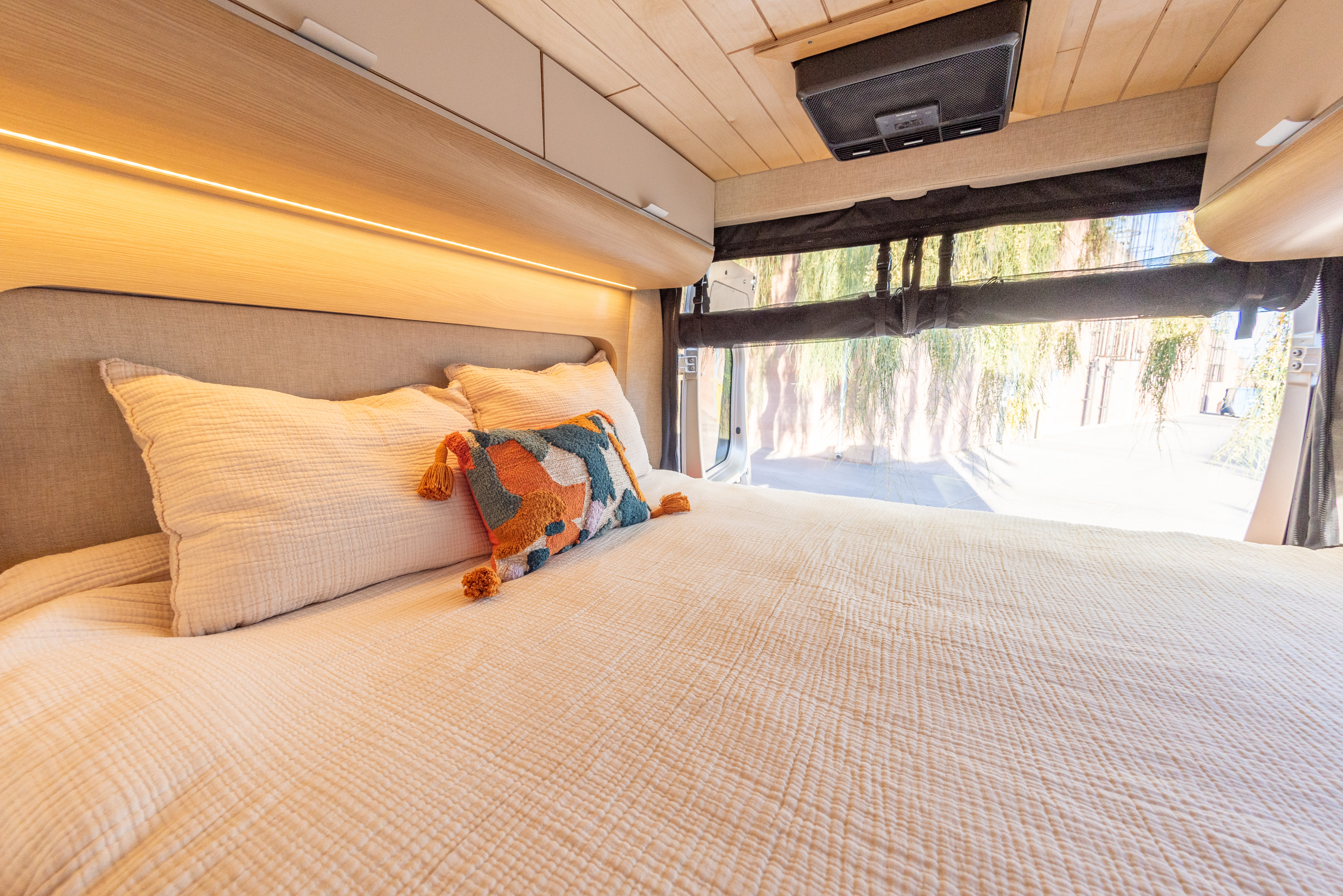 Comfortable RV rental interior featuring a cozy bed with ambient lighting, overhead storage, and outdoor views through the rear.. Noovo Lite 2023