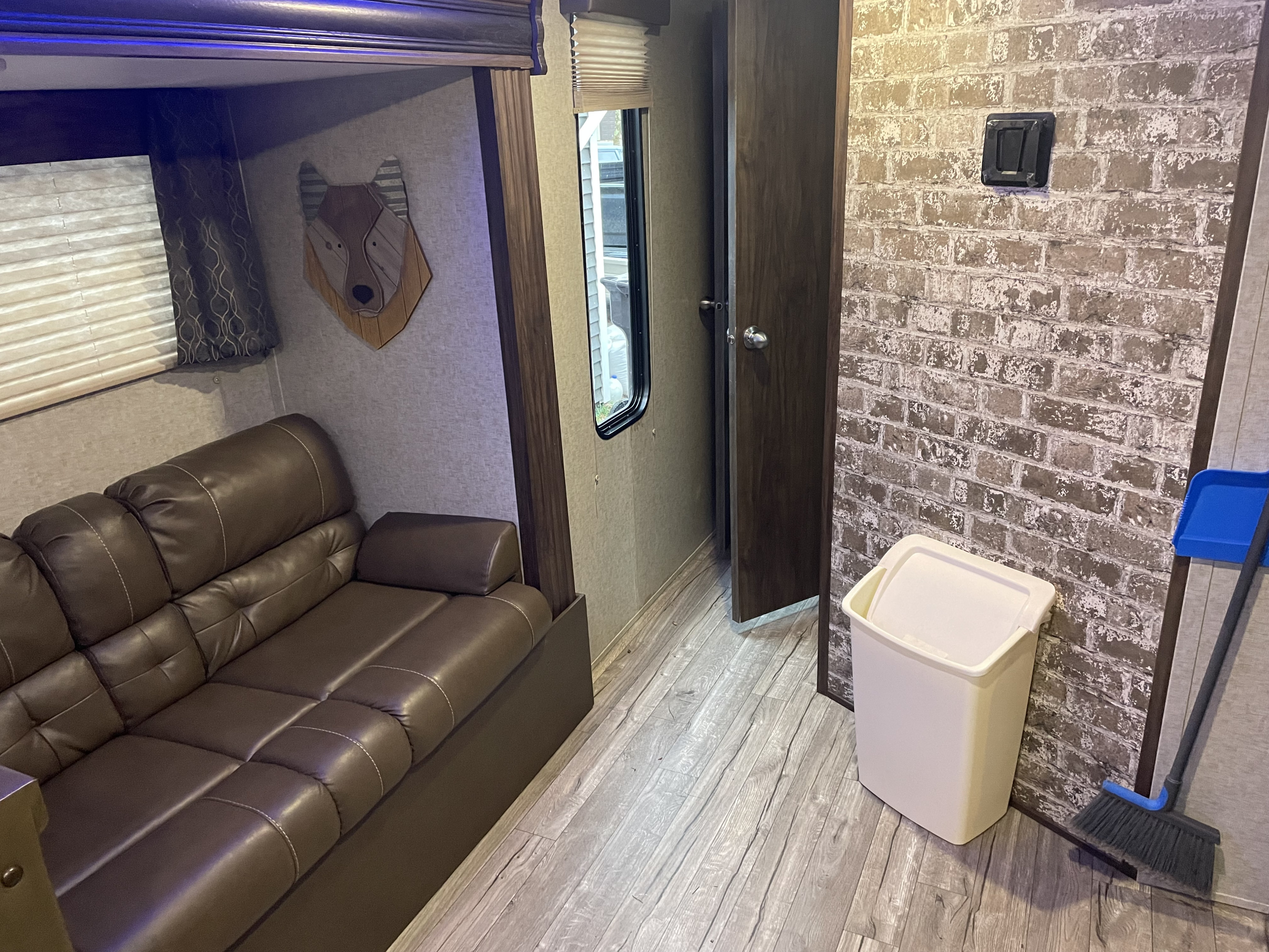 RV rental interior featuring a comfy brown leather sofa, bunk bed, window with blinds, and unique wolf wall art on patterned wall.. Forest River Cherokee Grey Wolf 2019
