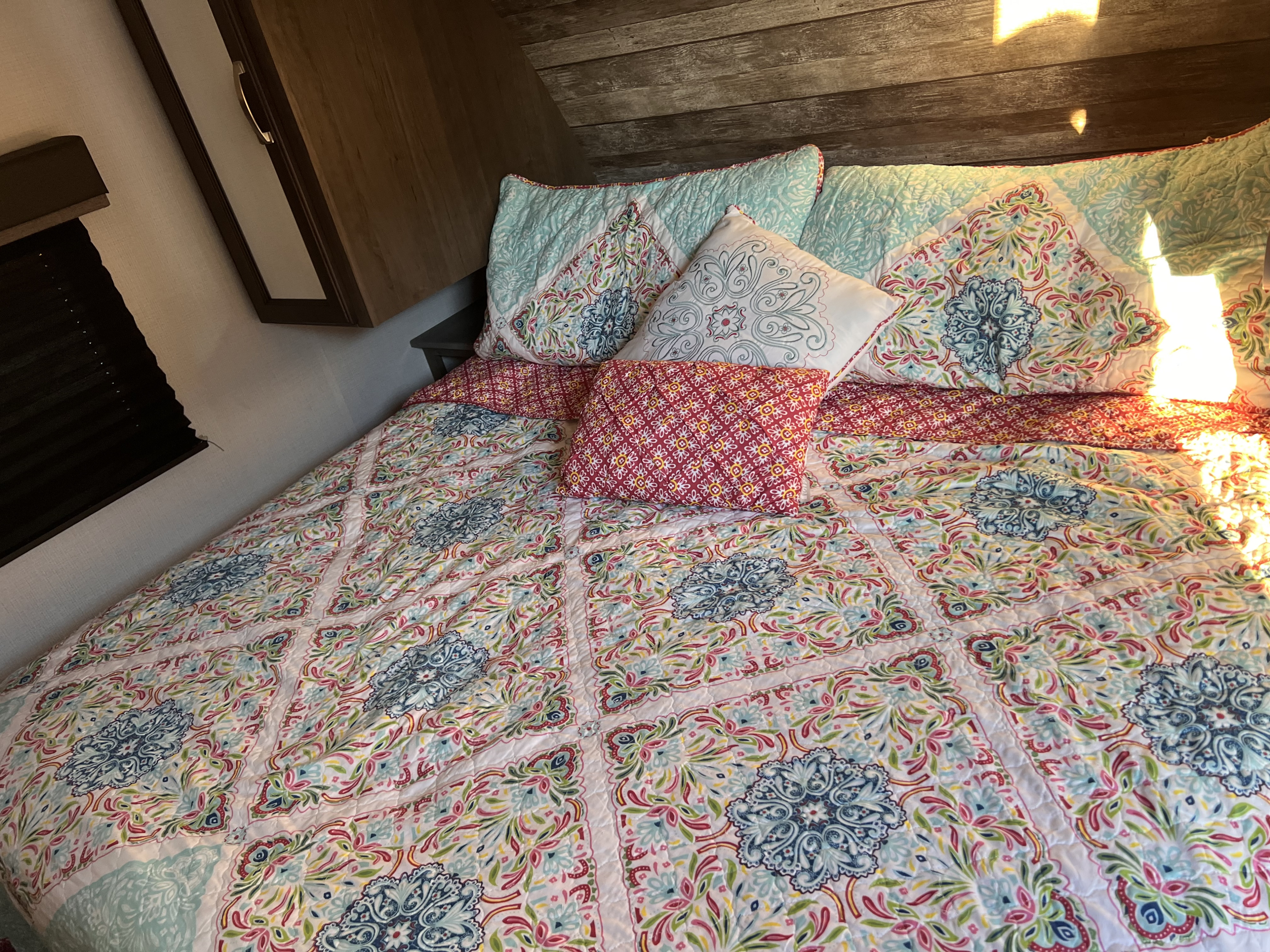 A cozy, patterned bed setup inside an RV rental, featuring a vibrant floral quilt and pillows. Ideal for comfortable travel.. Keystone RV Cougar 2021