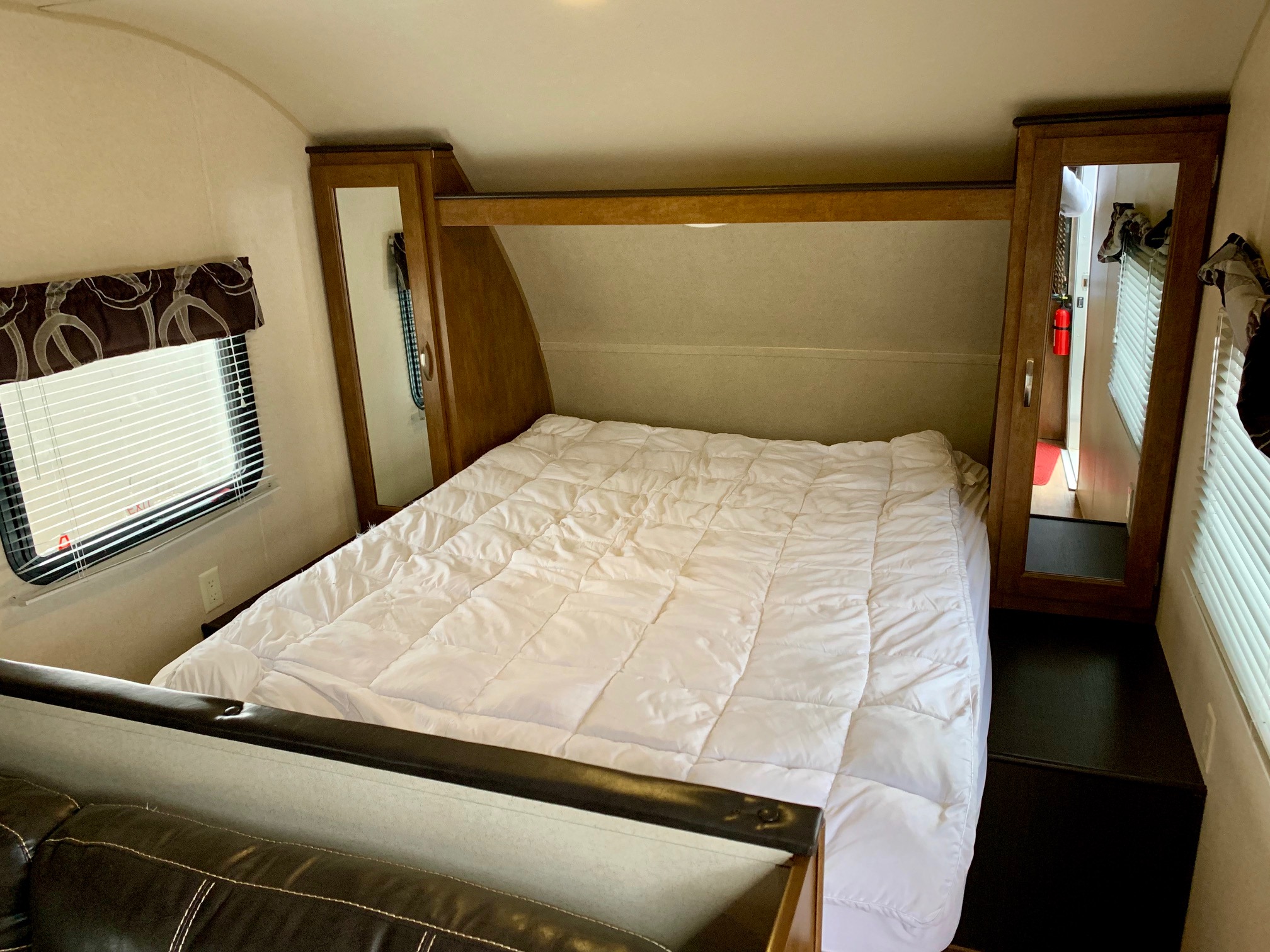 RV rental interior: A comfortable bedroom with a large bed, white comforter, wooden cabinets, and a window.. Forest River Cruise Lite 2017