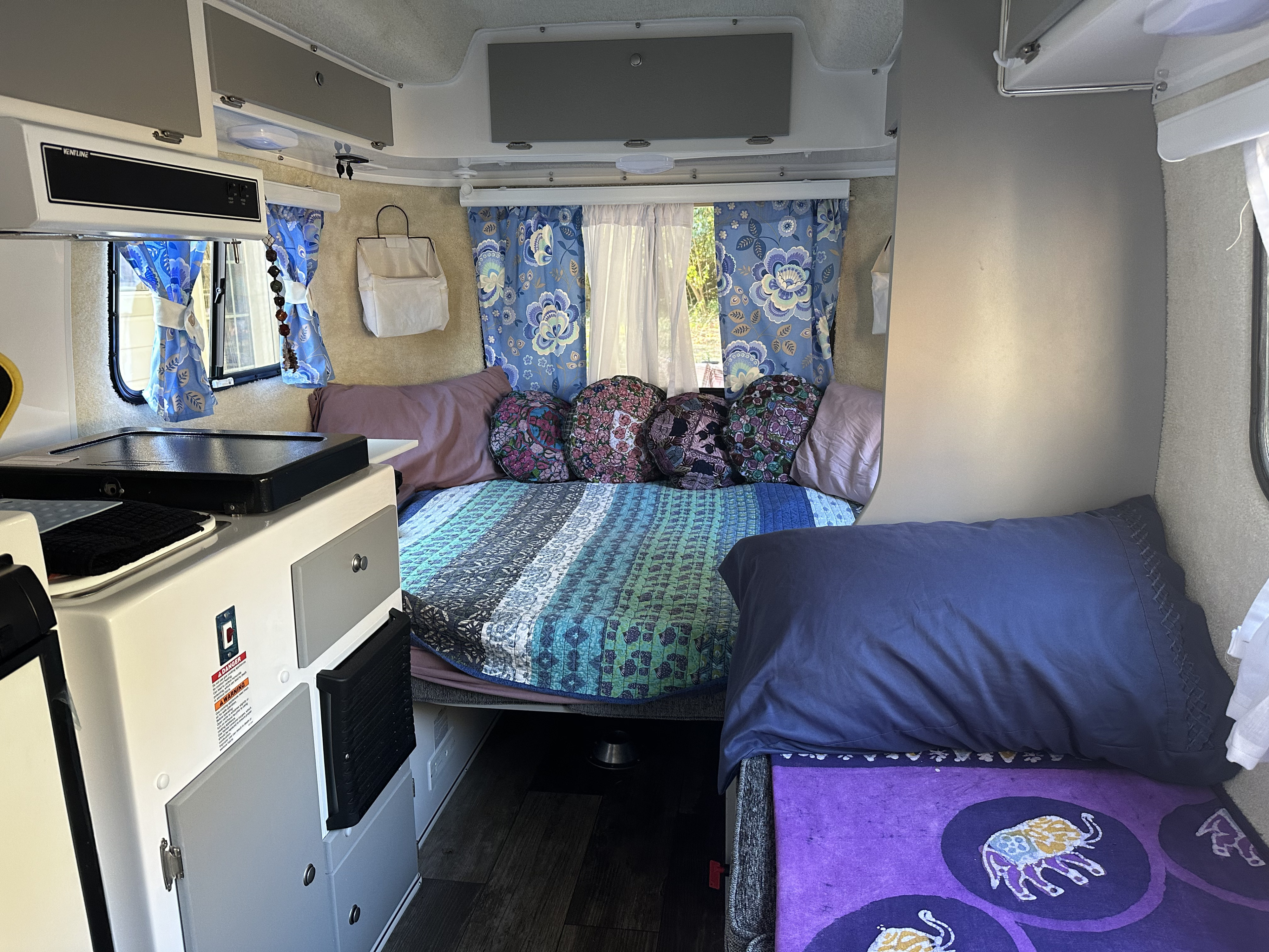 Cozy RV rental interior with a colorful bed, compact kitchen counter, and bright patterned curtains for comfortable travel.. Casita Spirit 2023