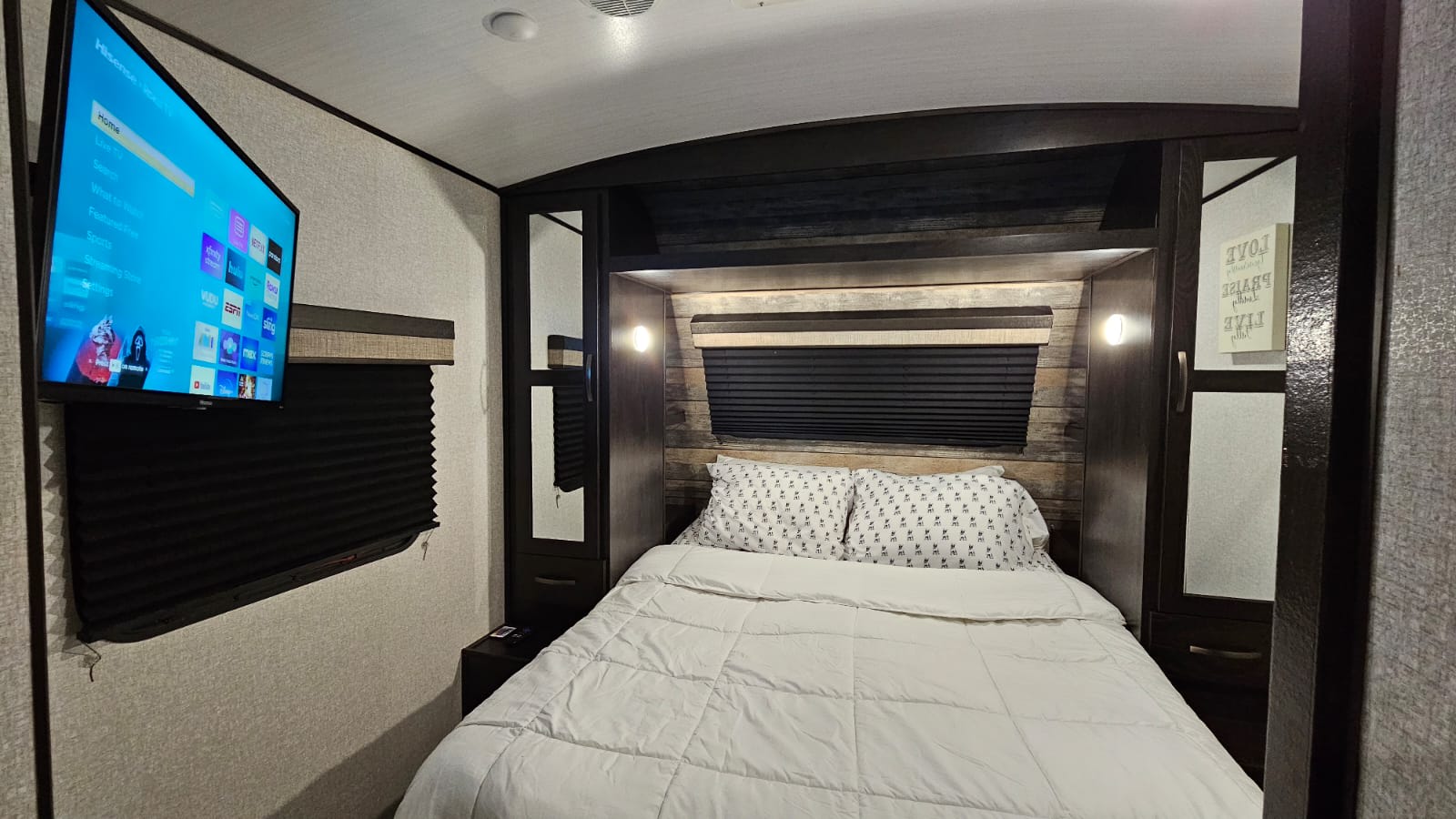 Cozy RV rental bedroom featuring a bed with white bedding, a decorative headboard, and a wall-mounted TV.. Forest River Surveyor Legend 2020
