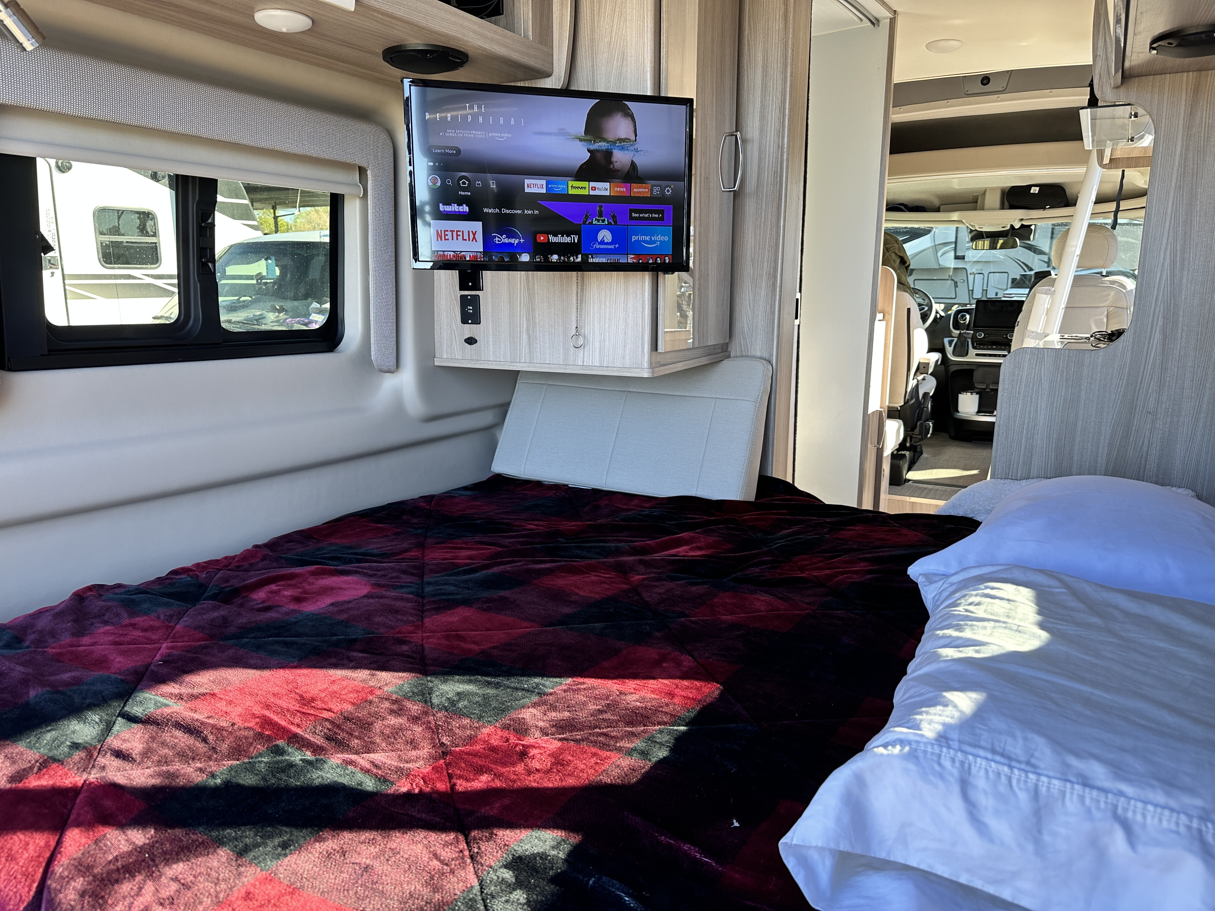 Relax in this RV rental with a cozy red plaid bed & TV showing "The Peripheral" and popular streaming apps.. Thor Sequnce 2023