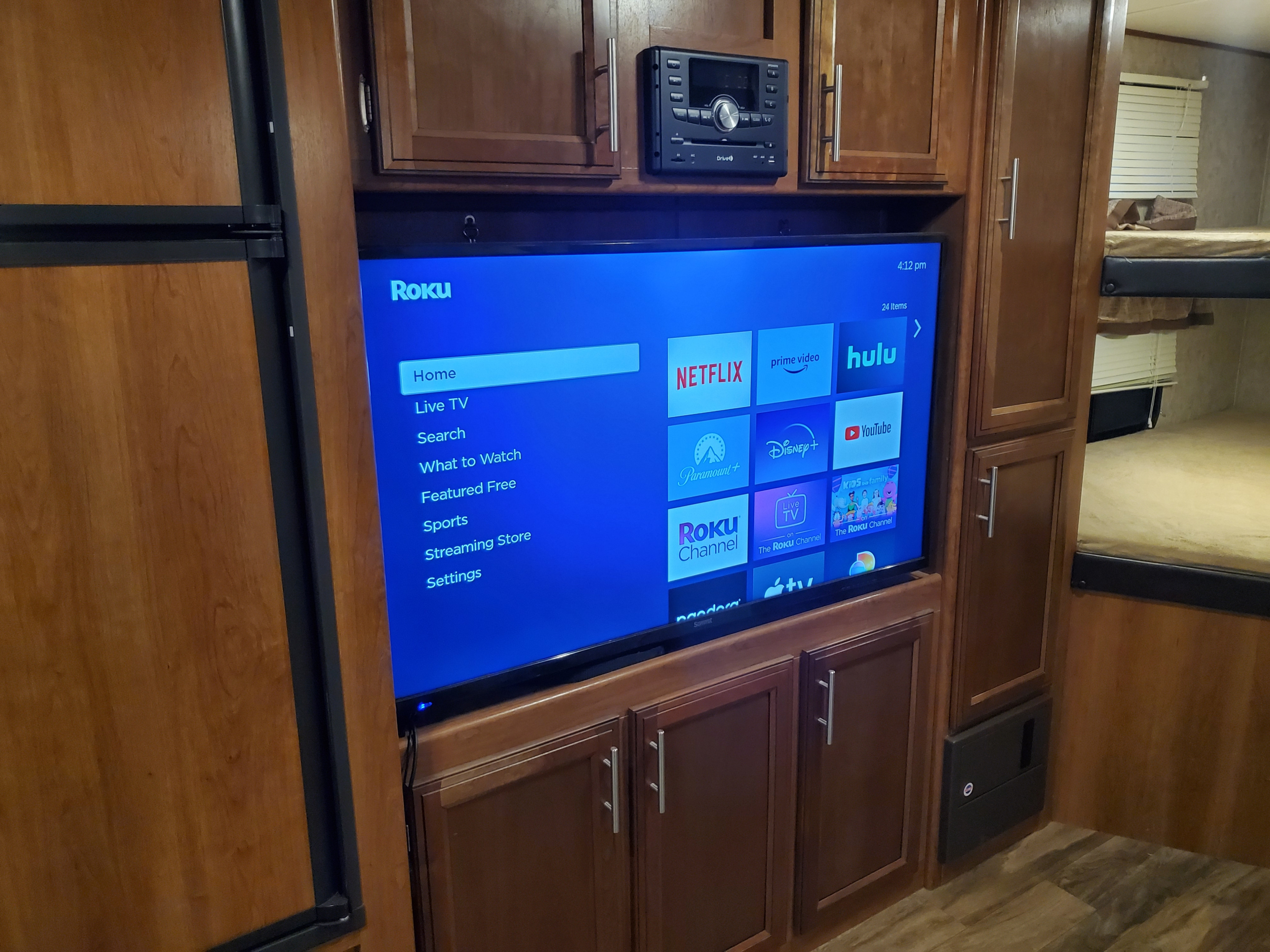 RV rental entertainment setup featuring a large Roku TV, built-in stereo, cabinets, and bunk beds in a cozy interior.. Prime Time Avenger 2018