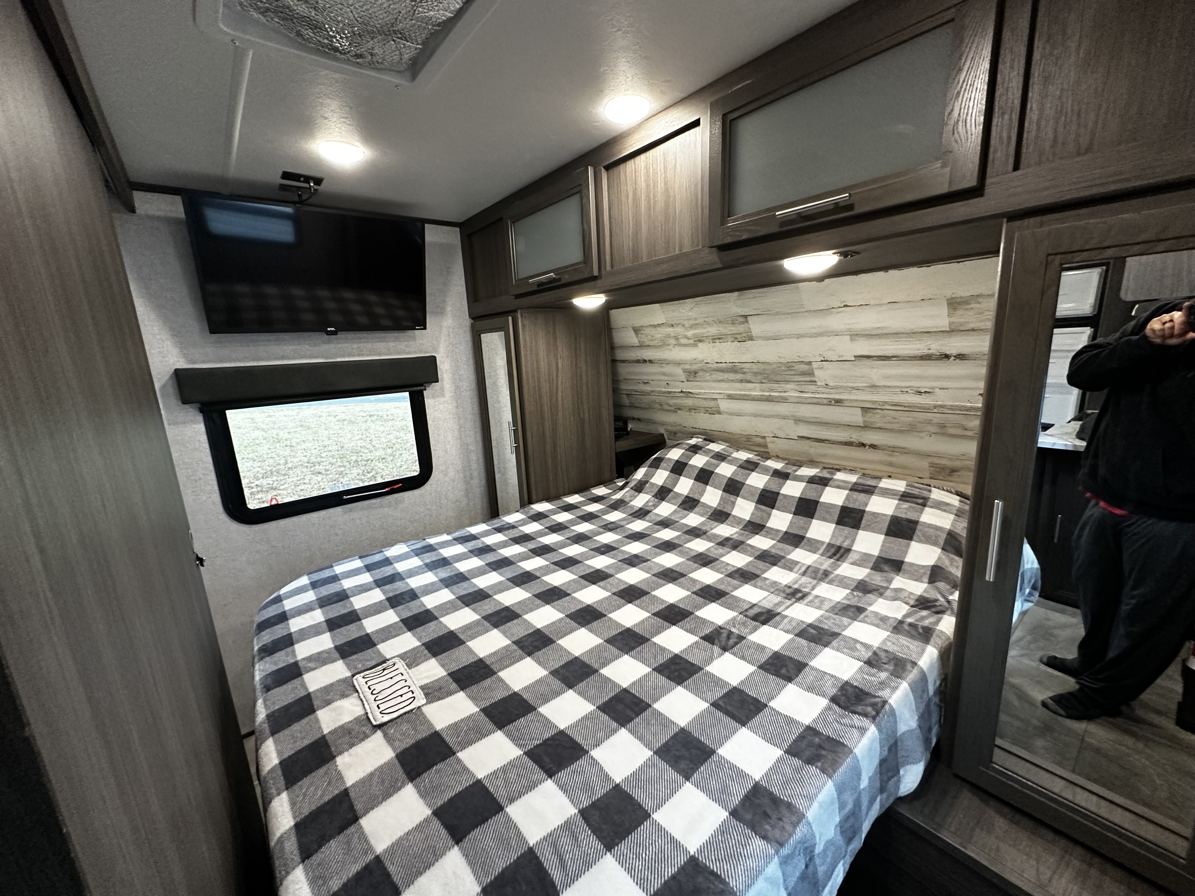 Inside a cozy RV rental bedroom: large bed with checkered blanket, wall-mounted TV, and window view.. Dutchmen Kodiak Ultra Lite 2021